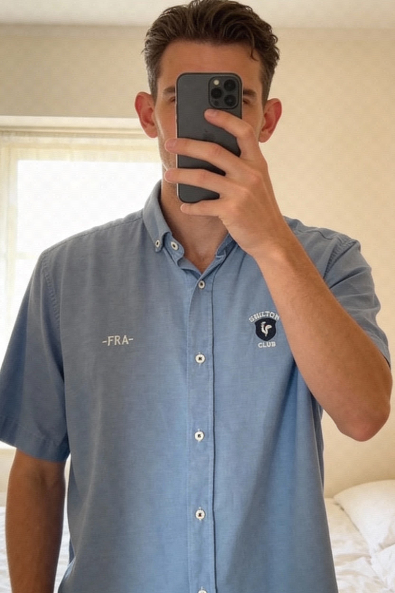 Chemise Shilton Club homme - Bleu - Taille M debout, face à la caméra, dans une chambre à la lumière douce, avec une lumière naturelle filtrant par la fenêtre.