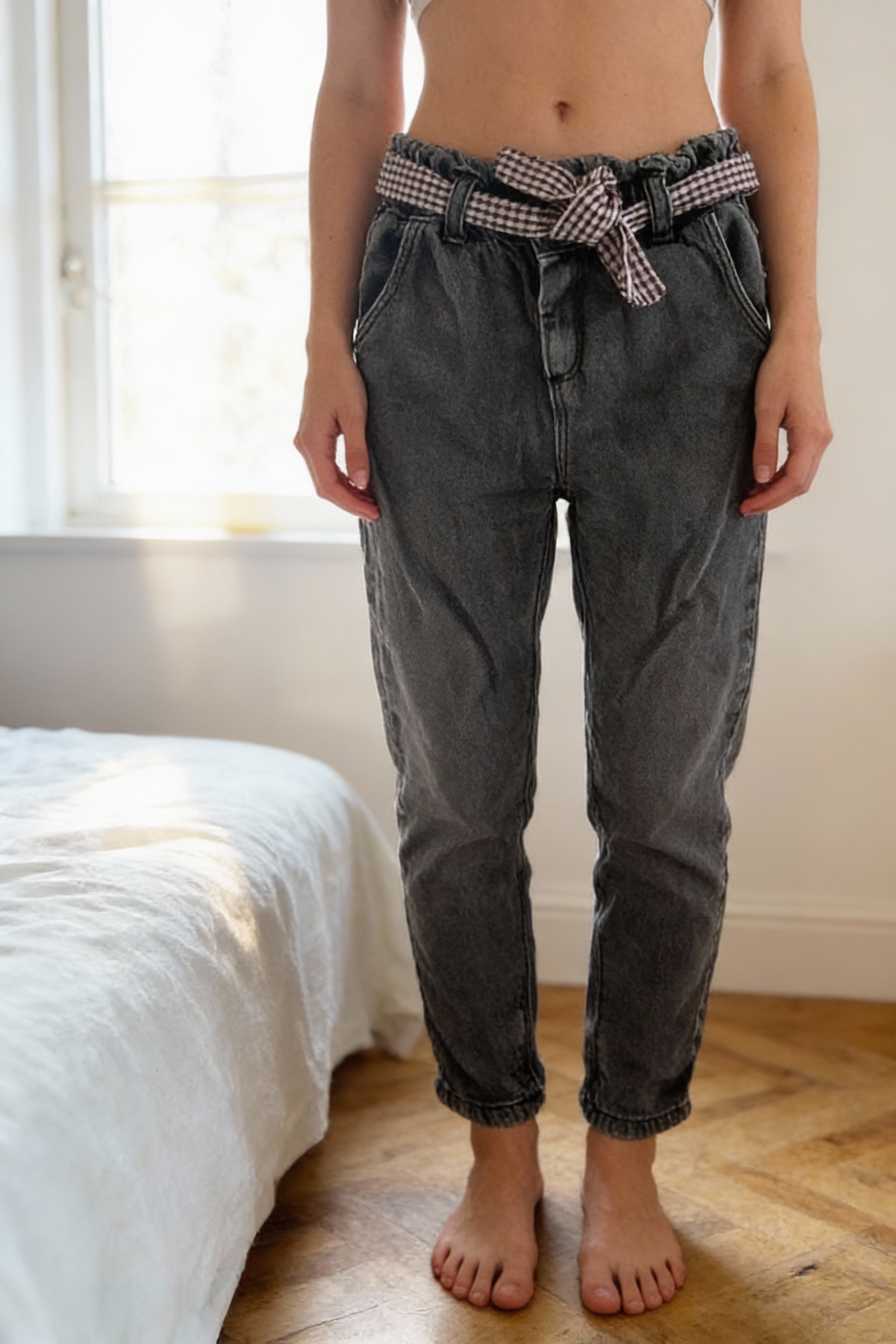 Zara Jeans aufrecht stehend, der Kamera zugewandt, in einem sanft beleuchteten Schlafzimmer, mit natürlichem Licht, das durch ein Fenster fällt.