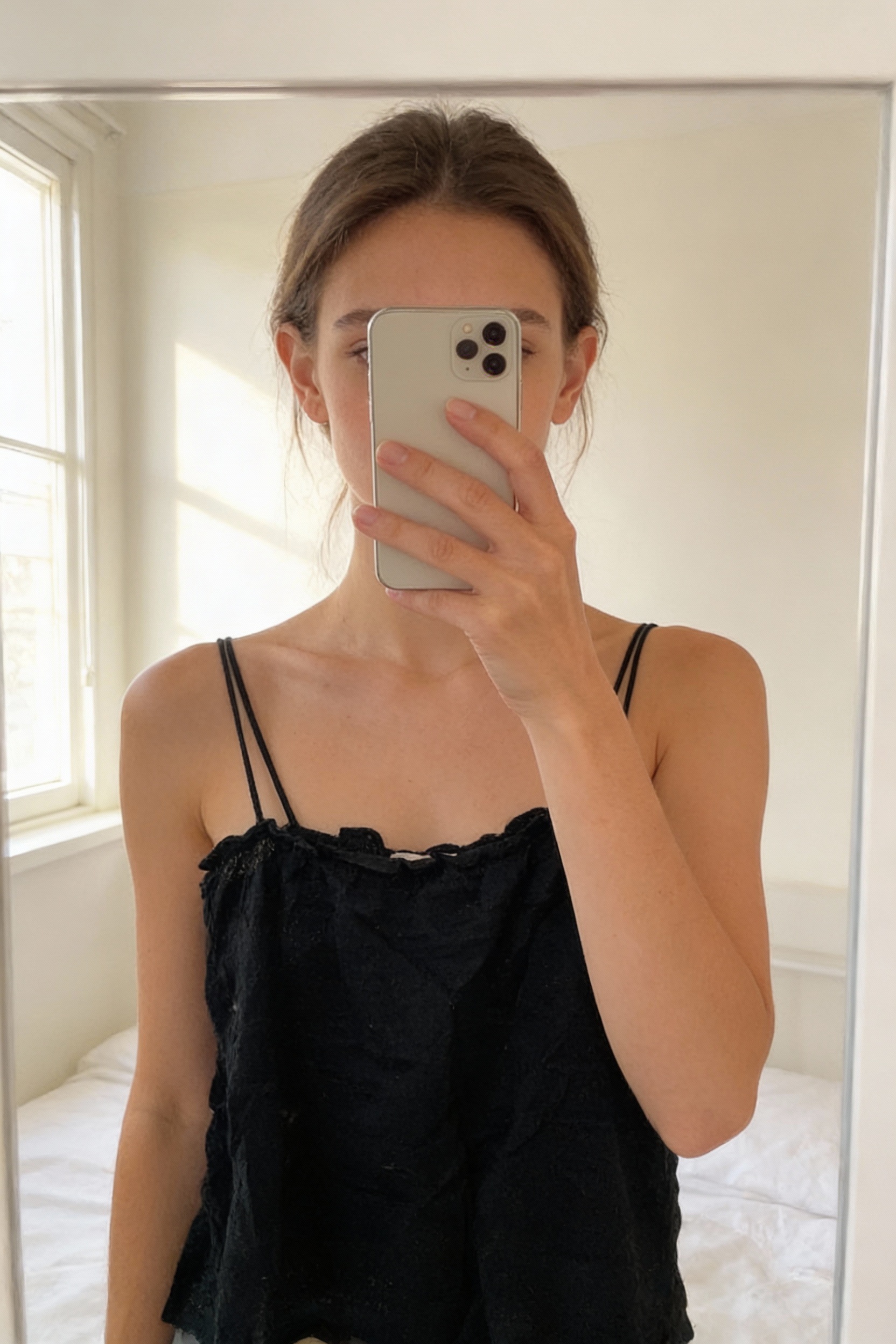 Débardeur Sezane debout, face à la caméra, dans une chambre à la lumière douce, avec une lumière naturelle filtrant par la fenêtre.