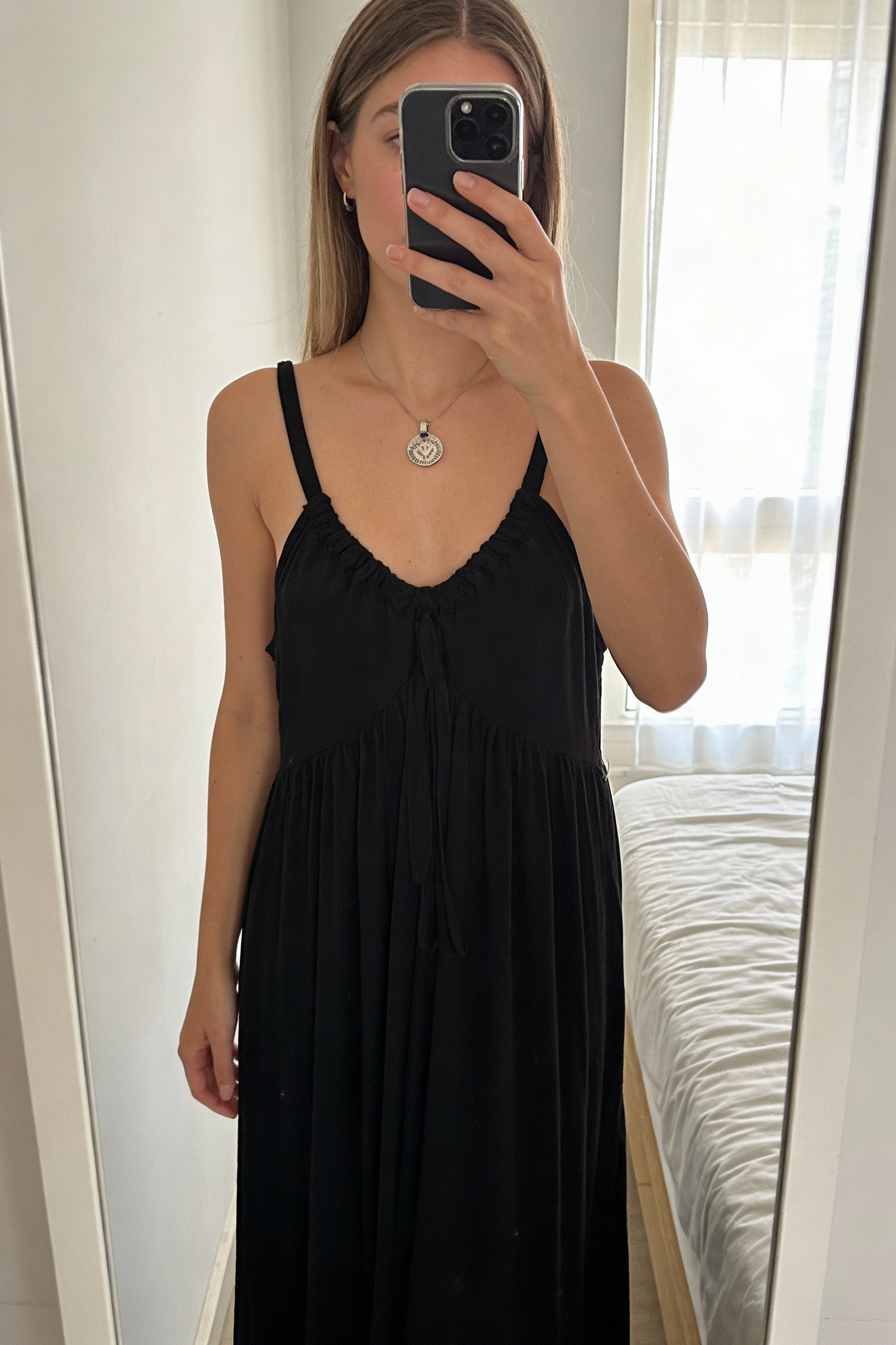 Robe Khujo noire XL debout, face à la caméra, dans une chambre à la lumière douce, avec une lumière naturelle filtrant par la fenêtre.