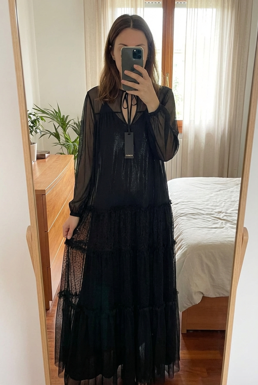 Black PINKO Transparent Maxi Dress in piedi, rivolto verso la fotocamera, in una camera da letto con luce soffusa e luce naturale che filtra dalla finestra.