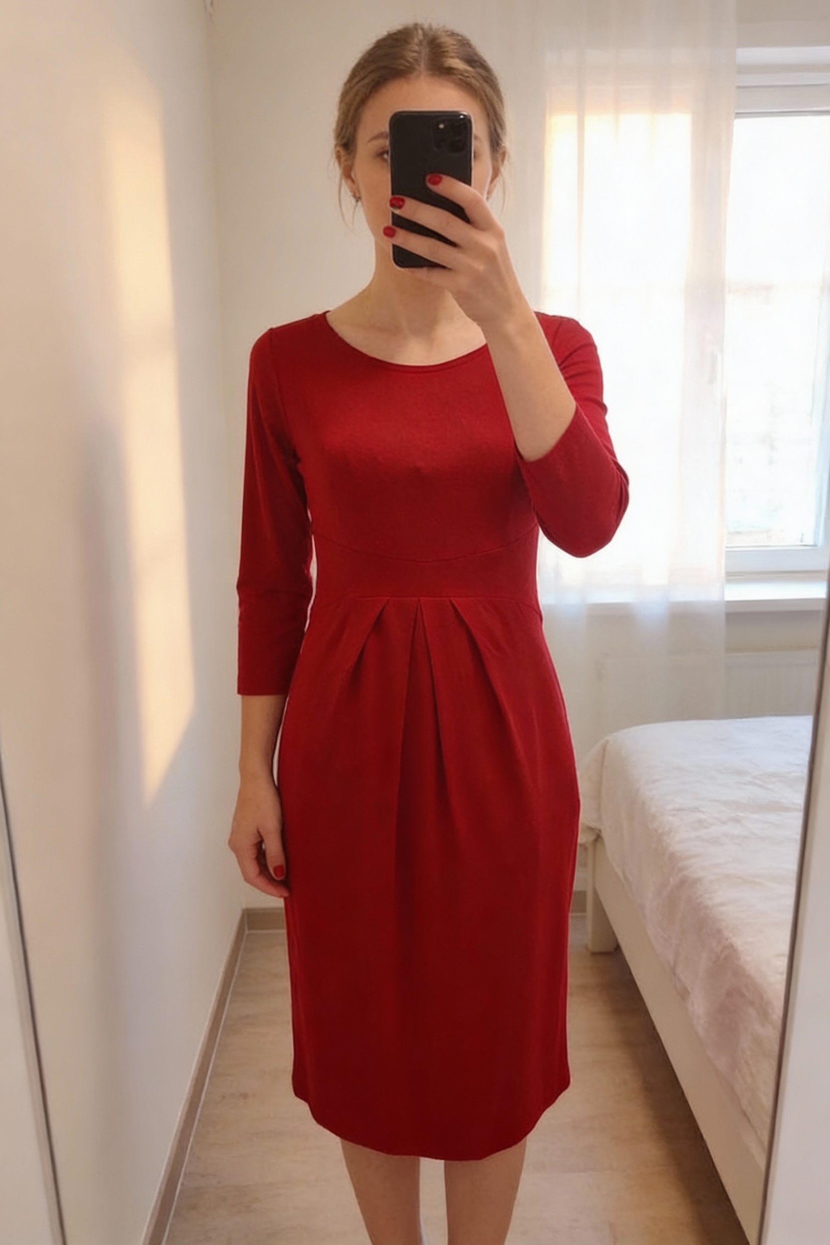 Maternity dress Isabella Oliver debout, face à la caméra, dans une chambre à la lumière douce, avec une lumière naturelle filtrant par la fenêtre.