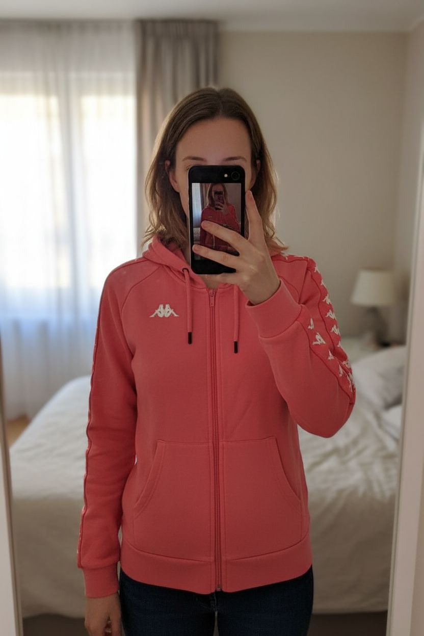 Felpa Kappa donna taglia M con logo frontale originale in piedi, rivolto verso la fotocamera, in una camera da letto con luce soffusa e luce naturale che filtra dalla finestra.