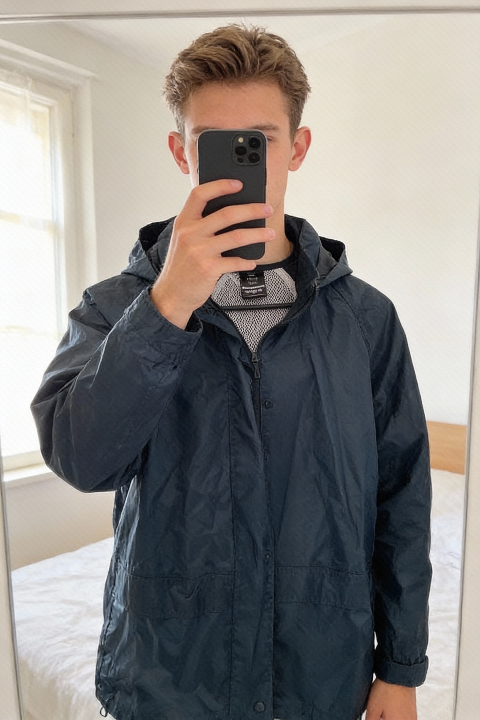 Imperméable coupe vent debout, face à la caméra, dans une chambre à la lumière douce, avec une lumière naturelle filtrant par la fenêtre.