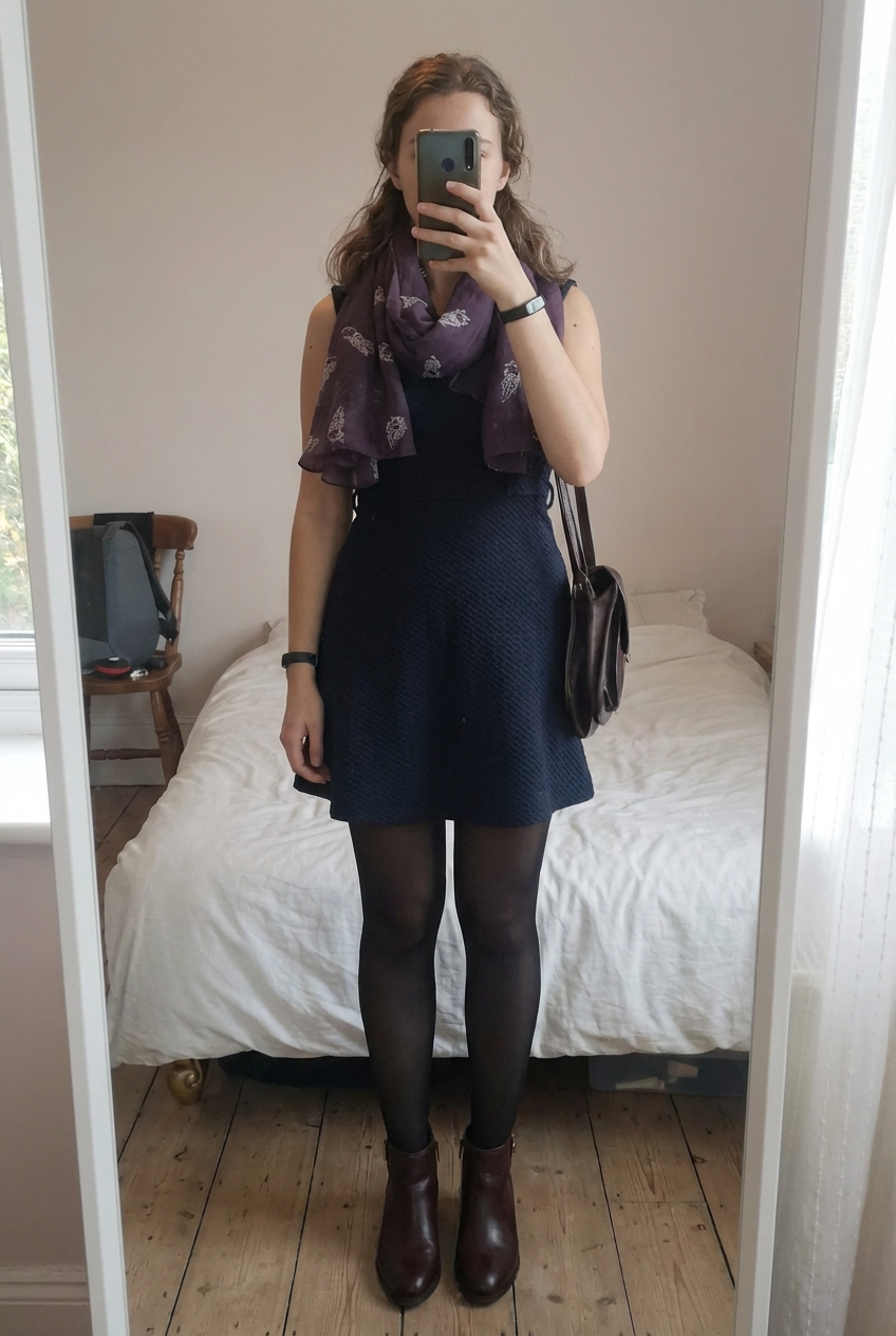 Vestido azul oscuro con textura de pie, mirando a la cámara, en un dormitorio con luz suave y natural filtrándose por la ventana.