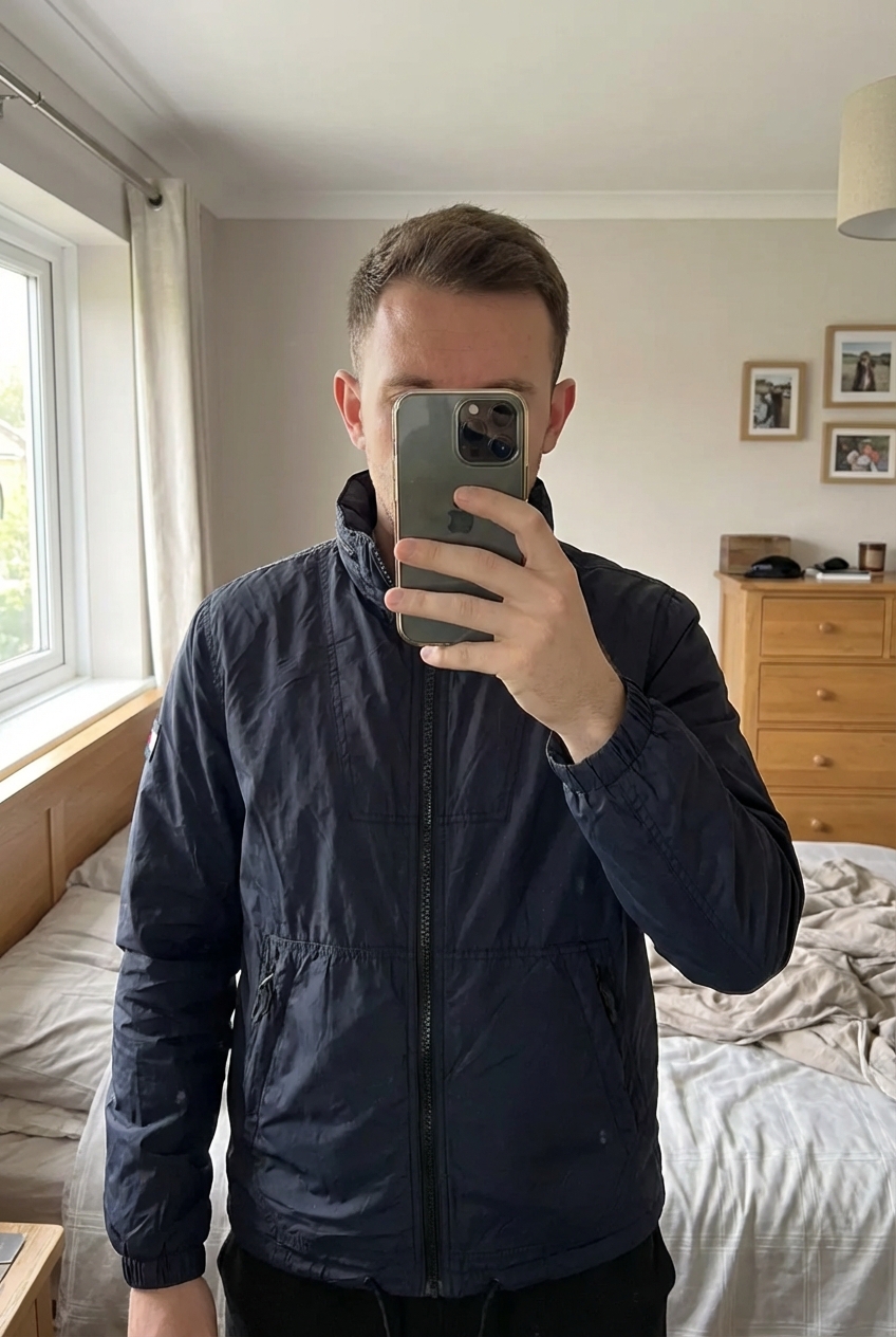 Tommy Hilfiger Navy Lightweight Zip Jacket – Logo Sleeve – Men’s standing straight facing the camera, in a softly lit bedroom setting, with gentle natural light filtering through a window.