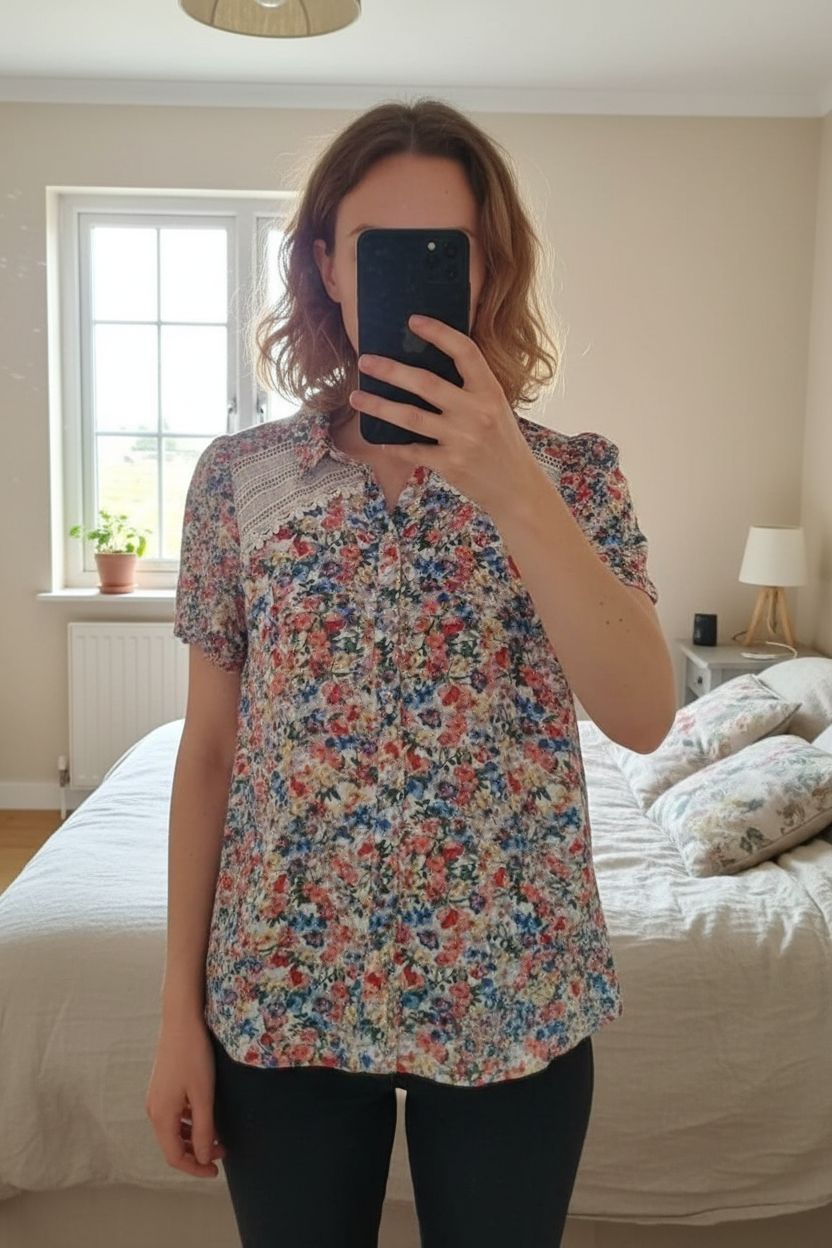 Blouse manches courtes debout, face à la caméra, dans une chambre à la lumière douce, avec une lumière naturelle filtrant par la fenêtre.