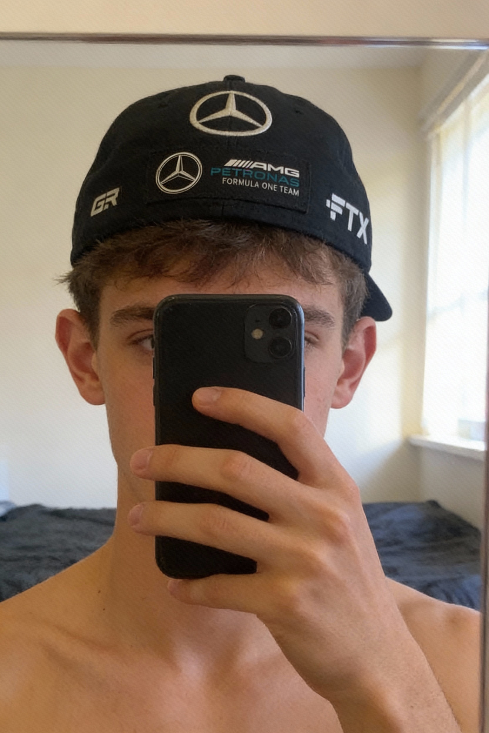 Casquette mercedes debout, face à la caméra, dans une chambre à la lumière douce, avec une lumière naturelle filtrant par la fenêtre.