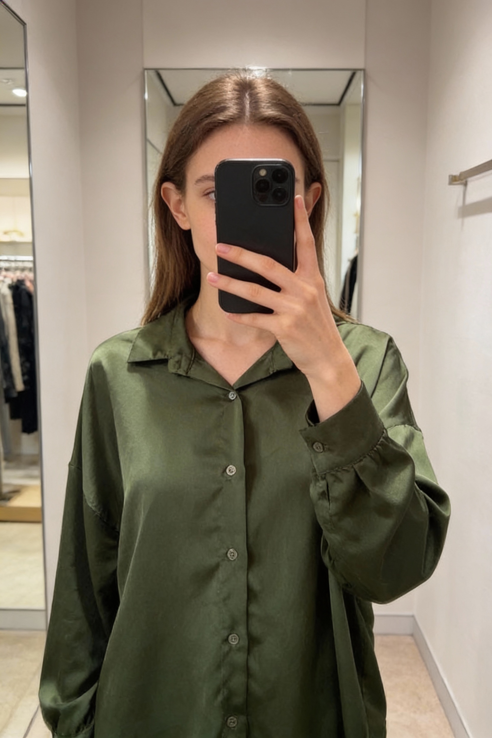 Una persona in Chemise verte femme M - Camicia donna M in piedi, rivolto verso la fotocamera, in un camerino in stile boutique con specchio e decorazioni neutre.