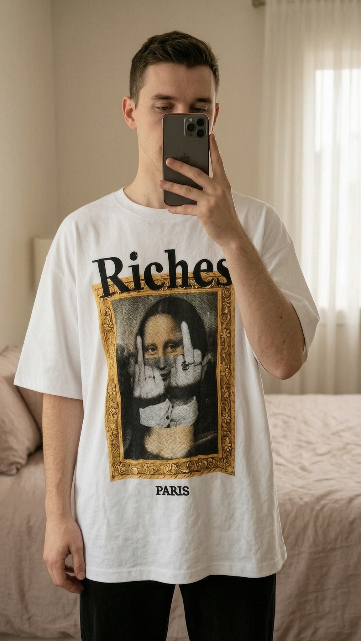 Tee-shirt Riche Paris neuf debout, face à la caméra, dans une chambre à la lumière douce, avec une lumière naturelle filtrant par la fenêtre.