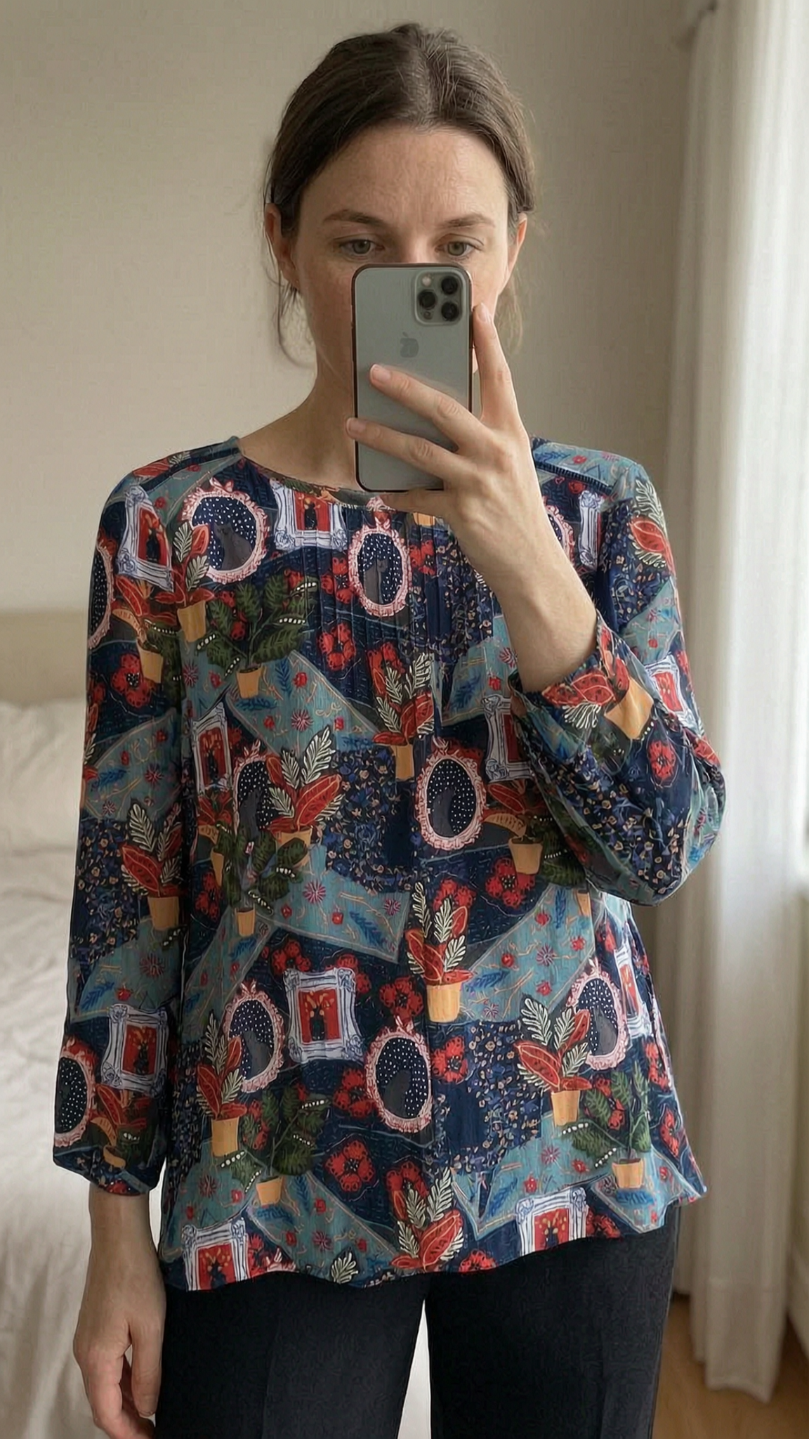 White Stuff blue colourful quirky print blouse - size 12 standing straight facing the camera, in a softly lit bedroom setting, with gentle natural light filtering through a window.