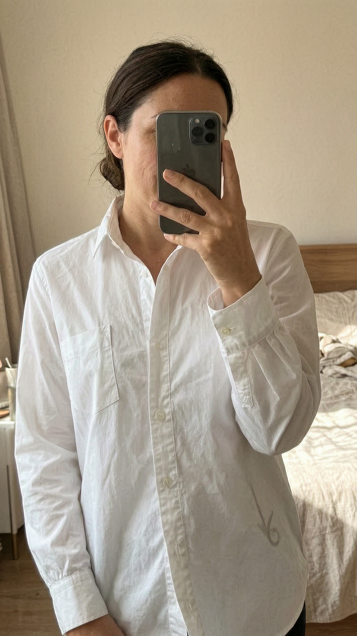 Eine Person in H&M Bluse Weiß Klassisch Größe 38 /M🤍 den Rücken leicht gewölbt für eine dynamische Pose, in einem sanft beleuchteten Schlafzimmer, mit natürlichem Licht, das durch ein Fenster fällt.