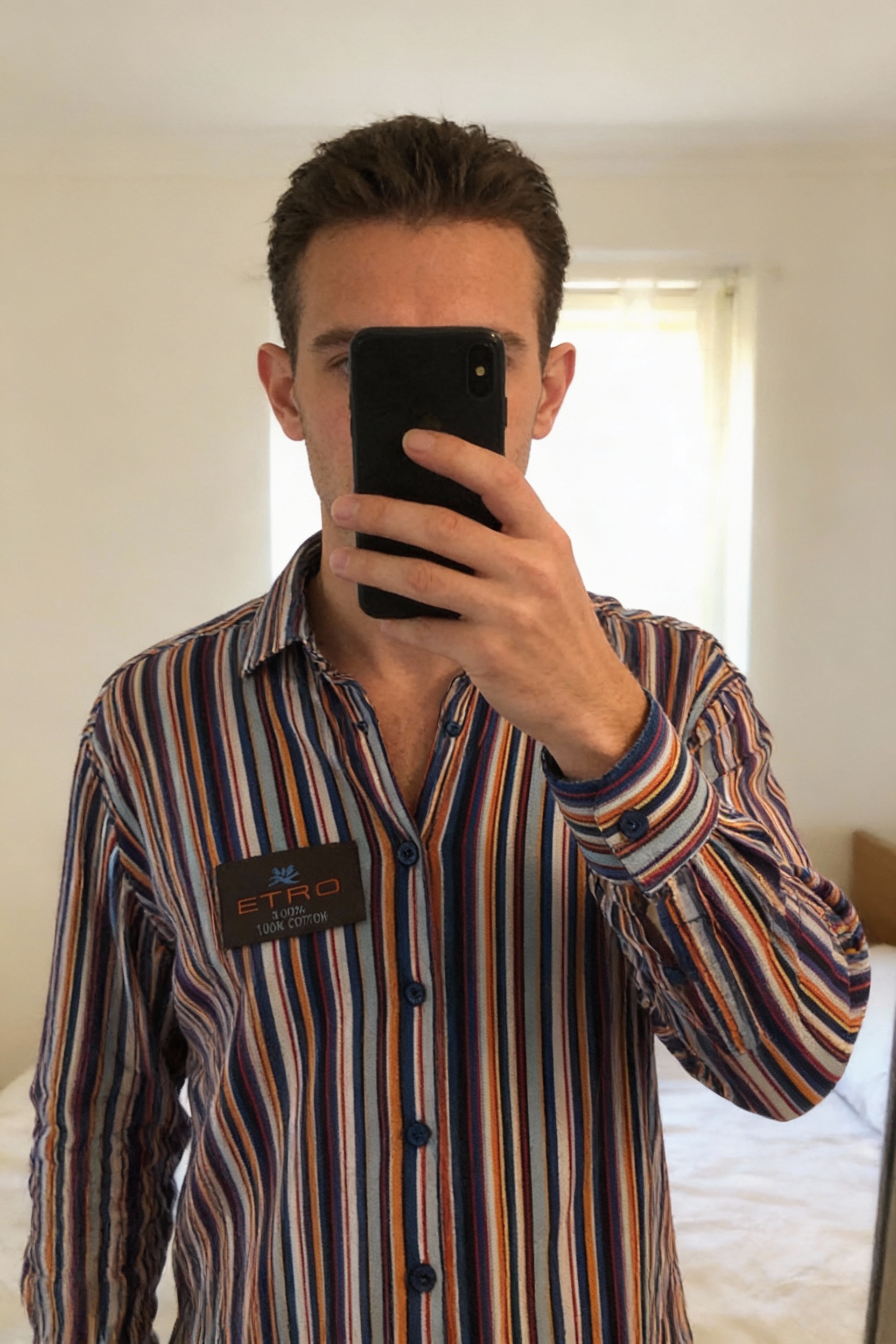 Chemise Etro Milano debout, face à la caméra, dans une chambre à la lumière douce, avec une lumière naturelle filtrant par la fenêtre.