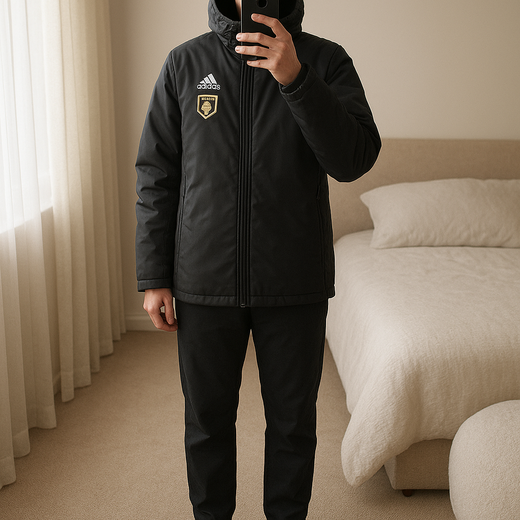 Casaco comprido adidas tamanho M mas veste grande em pé, de frente para a câmera, em um quarto com iluminação suave e luz natural filtrando pela janela.