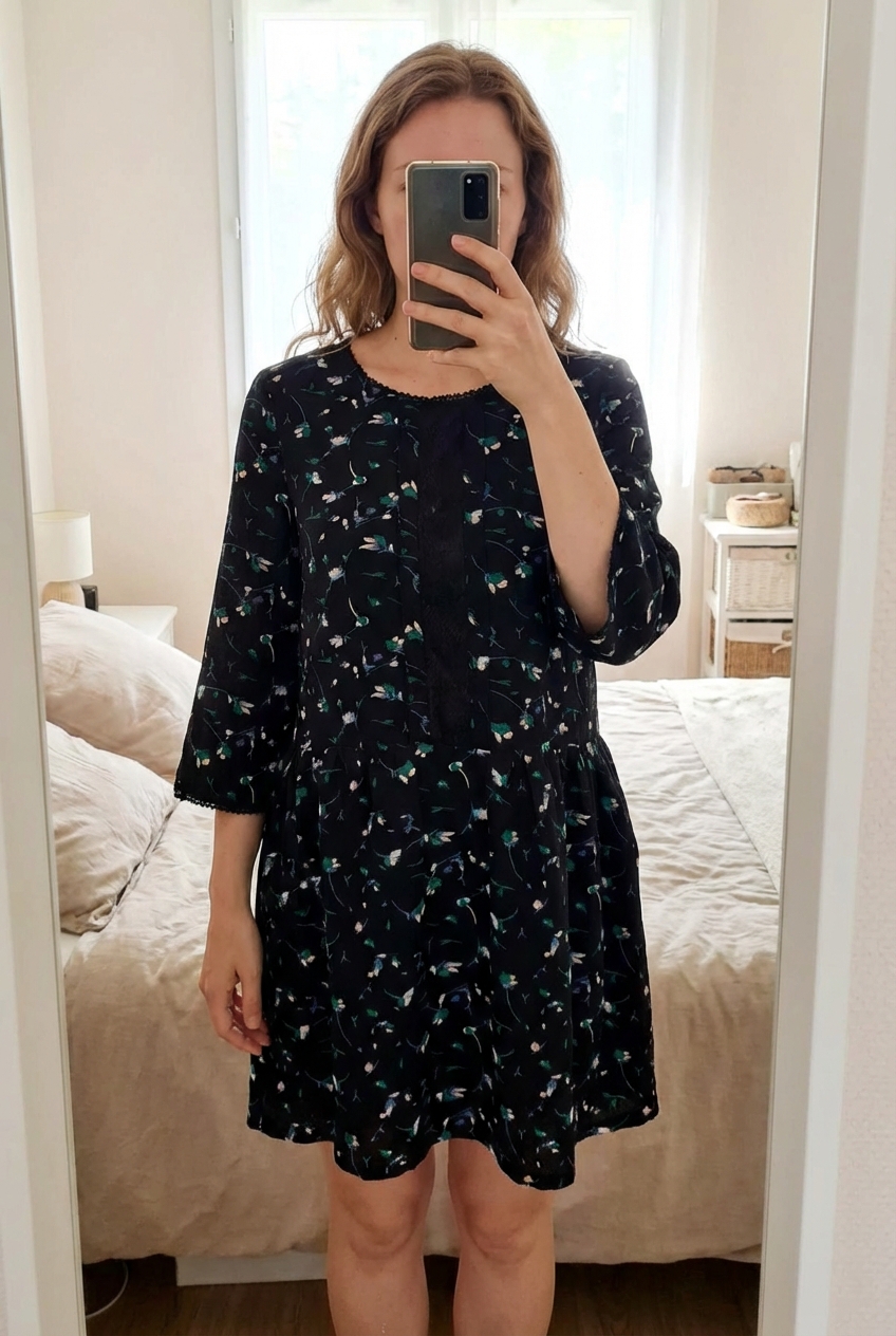 Une personne en Robe fleurie avec décolleté transparent - femme - L - Orfeo Paris debout, face à la caméra, dans une chambre à la lumière douce, avec une lumière naturelle filtrant par la fenêtre.