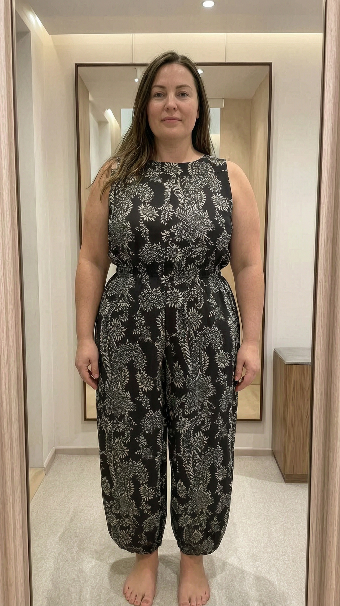 Une personne en Pantalon été, large, style Bohème, taille 38 debout, face à la caméra, avec une silhouette légèrement plus ronde, dans une cabine d’essayage de style boutique avec un miroir et une décoration neutre.