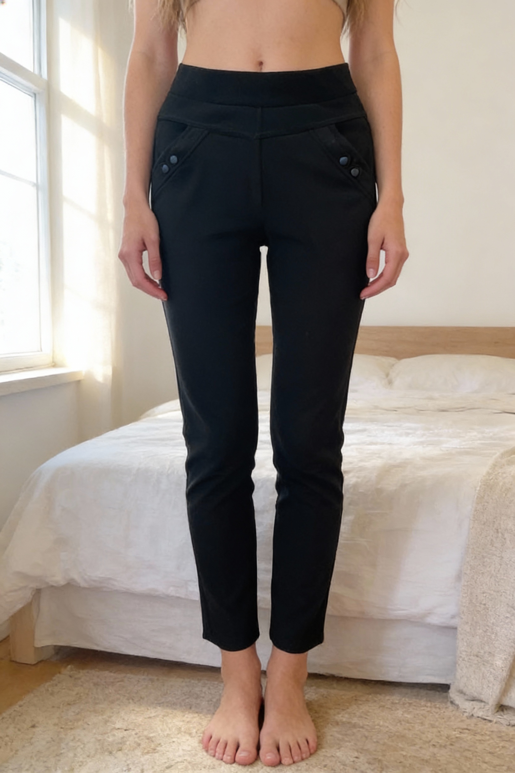 Legging femme noir taille 38 debout, face à la caméra, dans une chambre à la lumière douce, avec une lumière naturelle filtrant par la fenêtre.