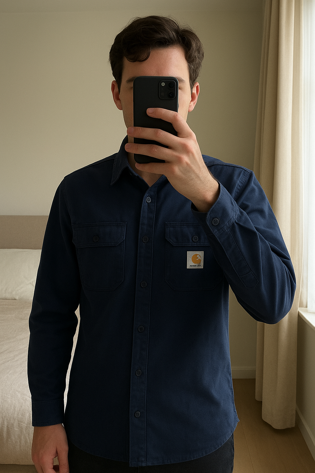 Sur chemise Carhartt bleu marine debout, face à la caméra, dans une chambre à la lumière douce, avec une lumière naturelle filtrant par la fenêtre.