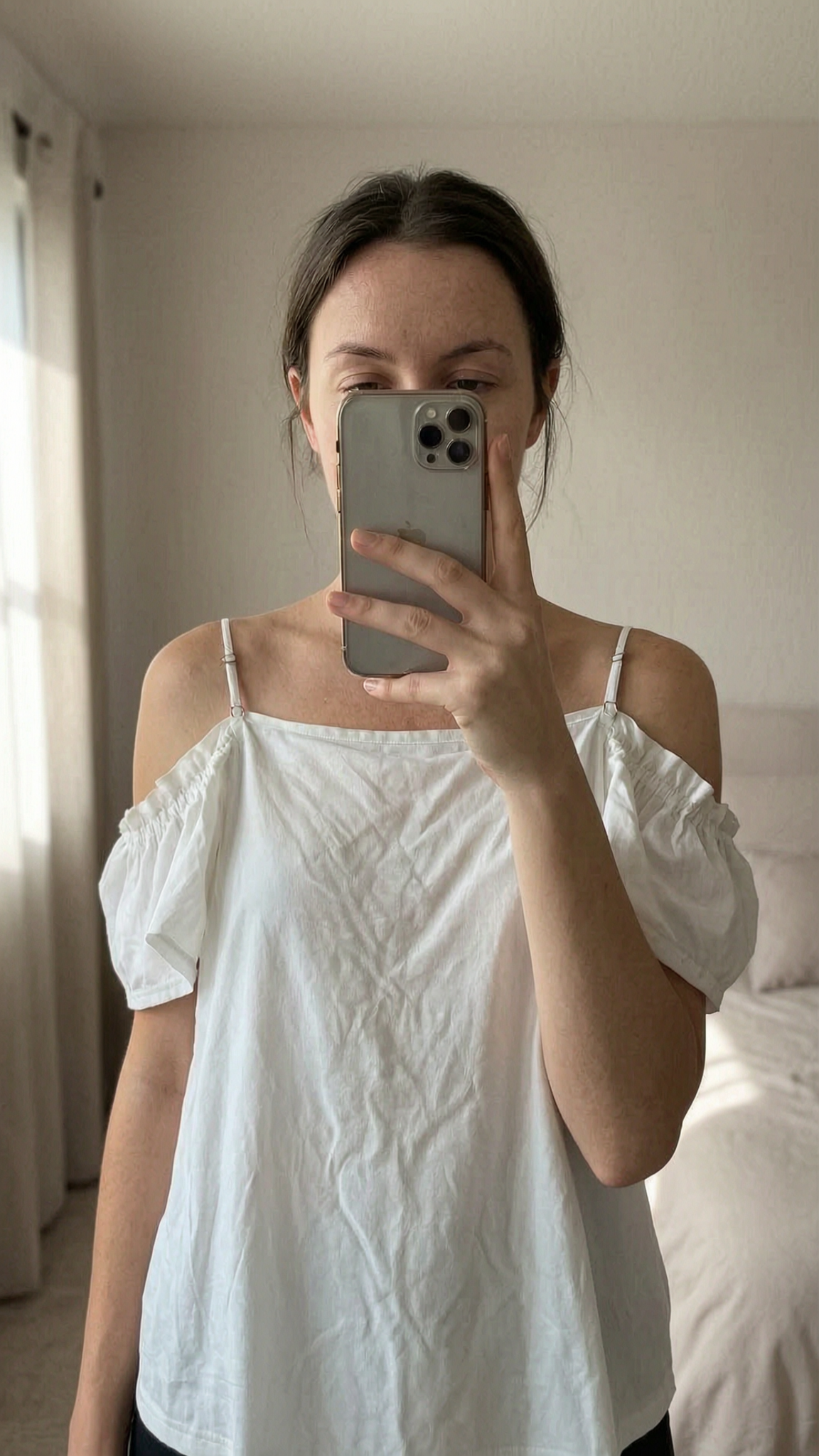 Haut épaules découvertes blanc L - Maglietta estate Donna L in piedi, rivolto verso la fotocamera, in una camera da letto con luce soffusa e luce naturale che filtra dalla finestra.