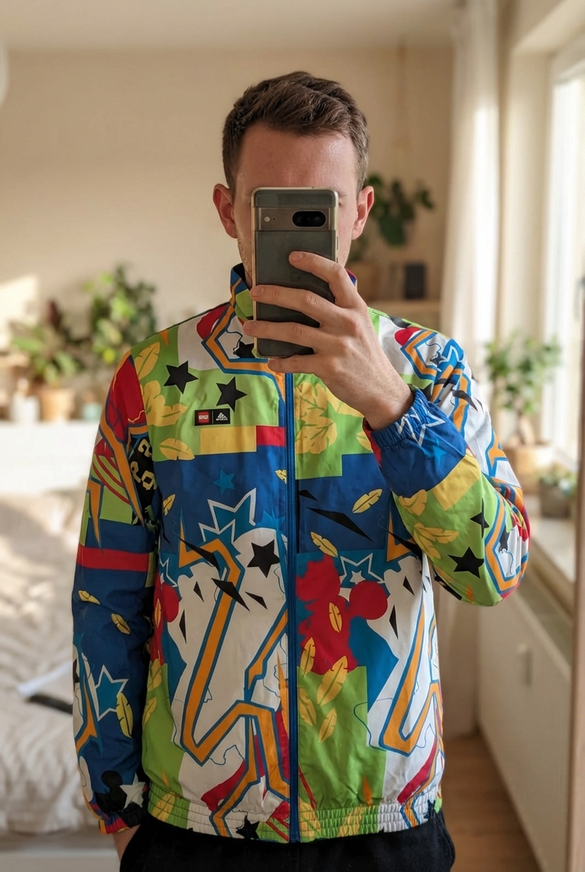 Veste Adidas Lego Tracksuit Set debout, face à la caméra, dans une chambre à la lumière douce, avec une lumière naturelle filtrant par la fenêtre.