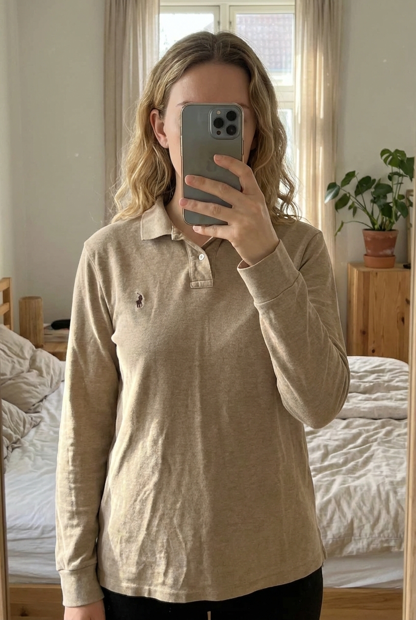 Polo Ralph lauren debout, face à la caméra, dans une chambre à la lumière douce, avec une lumière naturelle filtrant par la fenêtre.