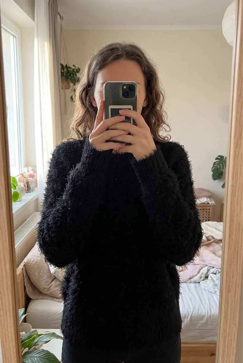 Pull noir hiver femme L - Maglione invernali donna L in piedi, rivolto verso la fotocamera, in una camera da letto con luce soffusa e luce naturale che filtra dalla finestra.