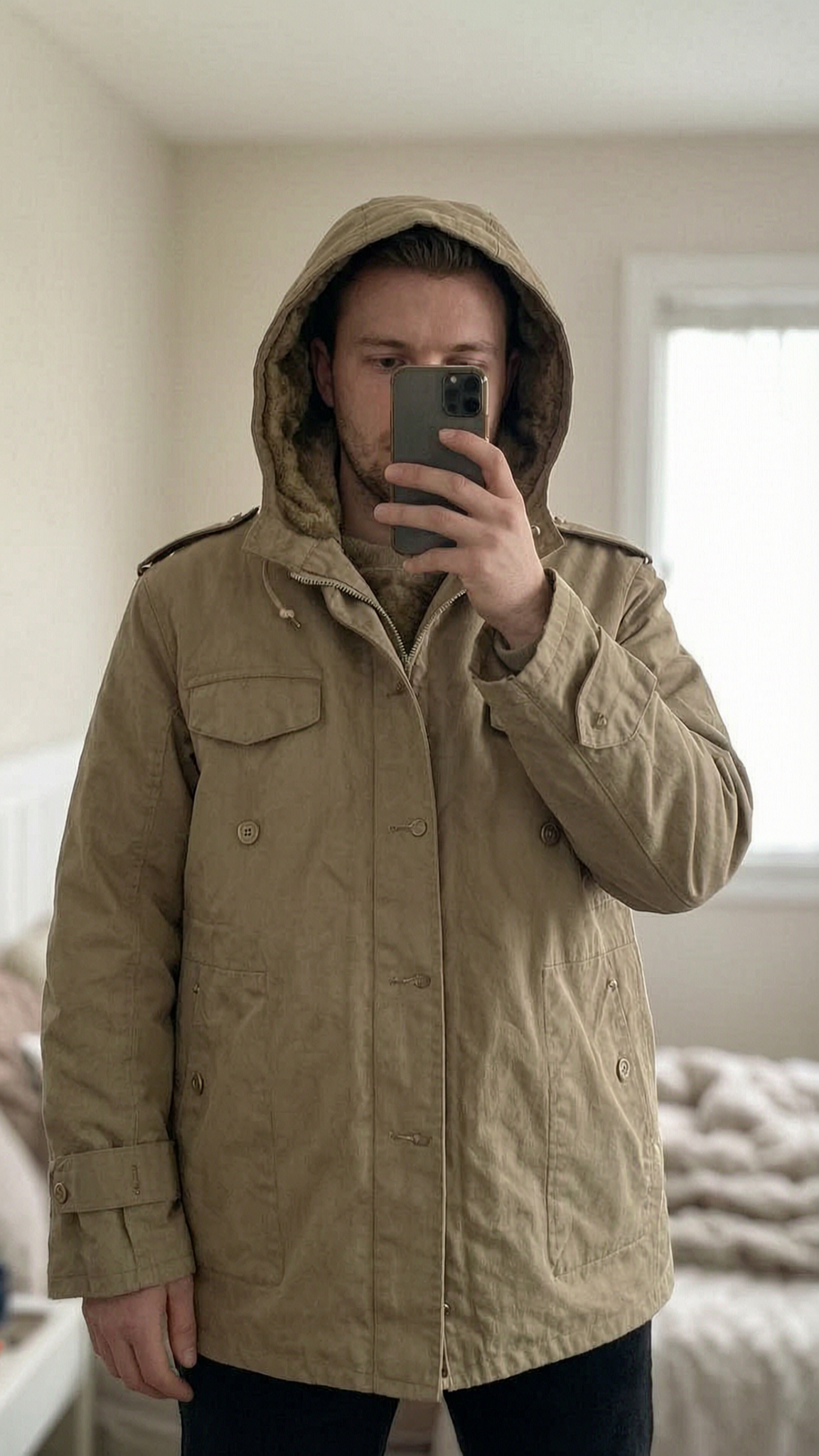 Vintage 90s Military Parka - Khaki / Tan - Fur Lined - Streetwear / Gorpcore - Size XL in piedi, rivolto verso la fotocamera, in una camera da letto con luce soffusa e luce naturale che filtra dalla finestra.