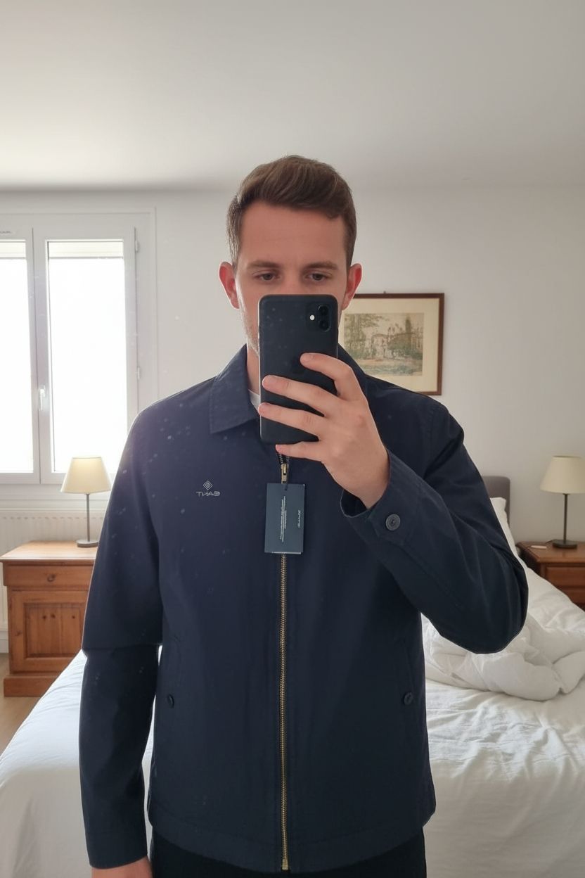 Veste homme Gant debout, face à la caméra, dans une chambre à la lumière douce, avec une lumière naturelle filtrant par la fenêtre.