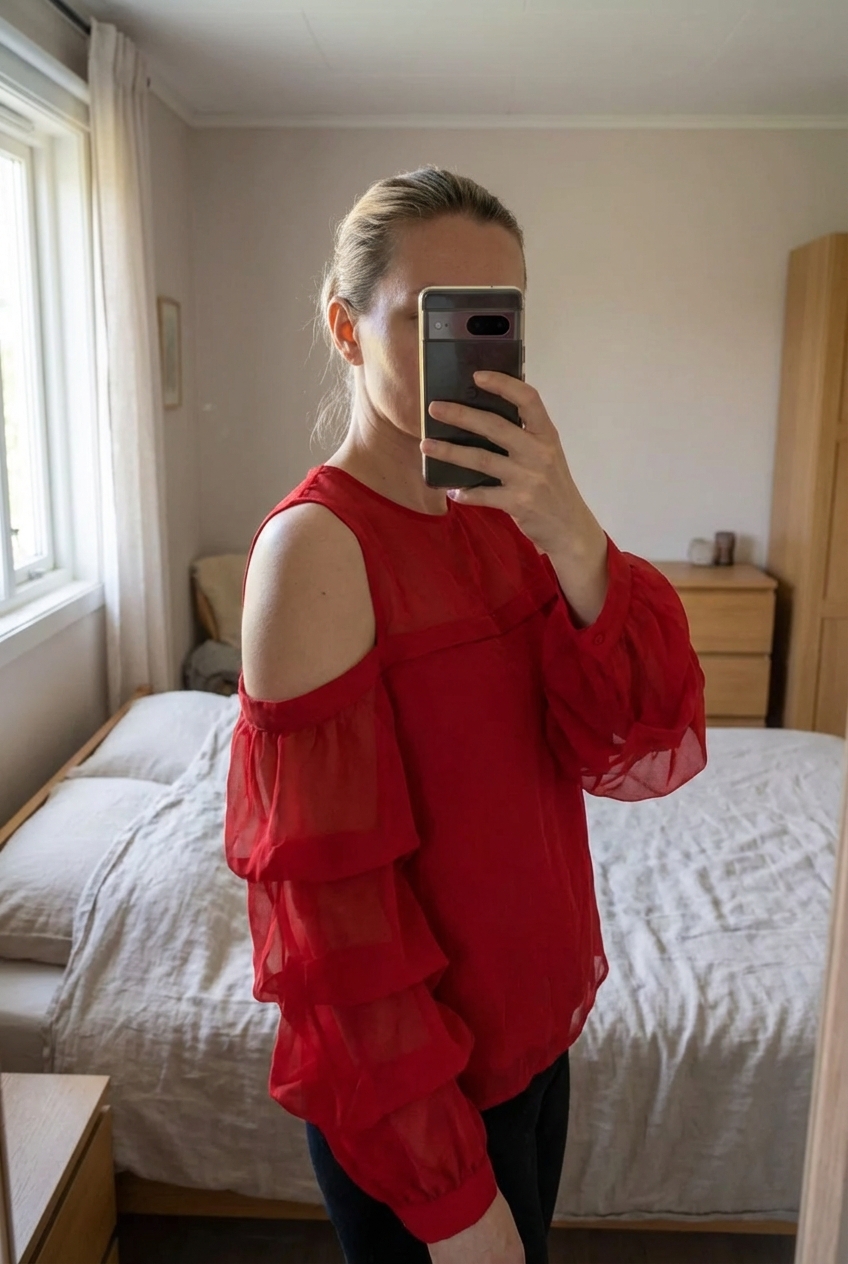 Haut rouge fluide H&M épaules dénudées et volants taille S debout, face à la caméra, dans une chambre à la lumière douce, avec une lumière naturelle filtrant par la fenêtre.