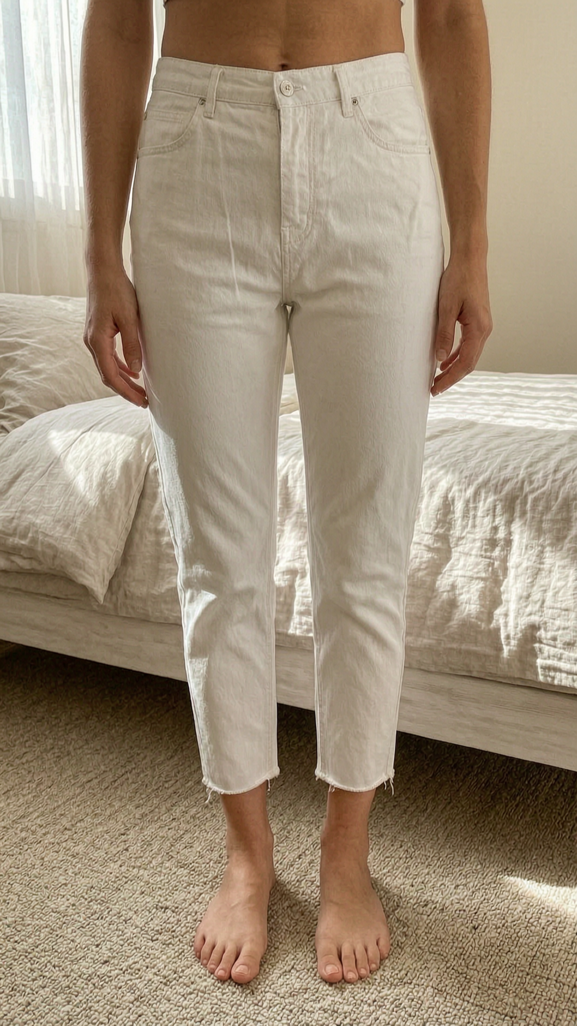 Jean iro blanc court debout, face à la caméra, dans une chambre à la lumière douce, avec une lumière naturelle filtrant par la fenêtre.