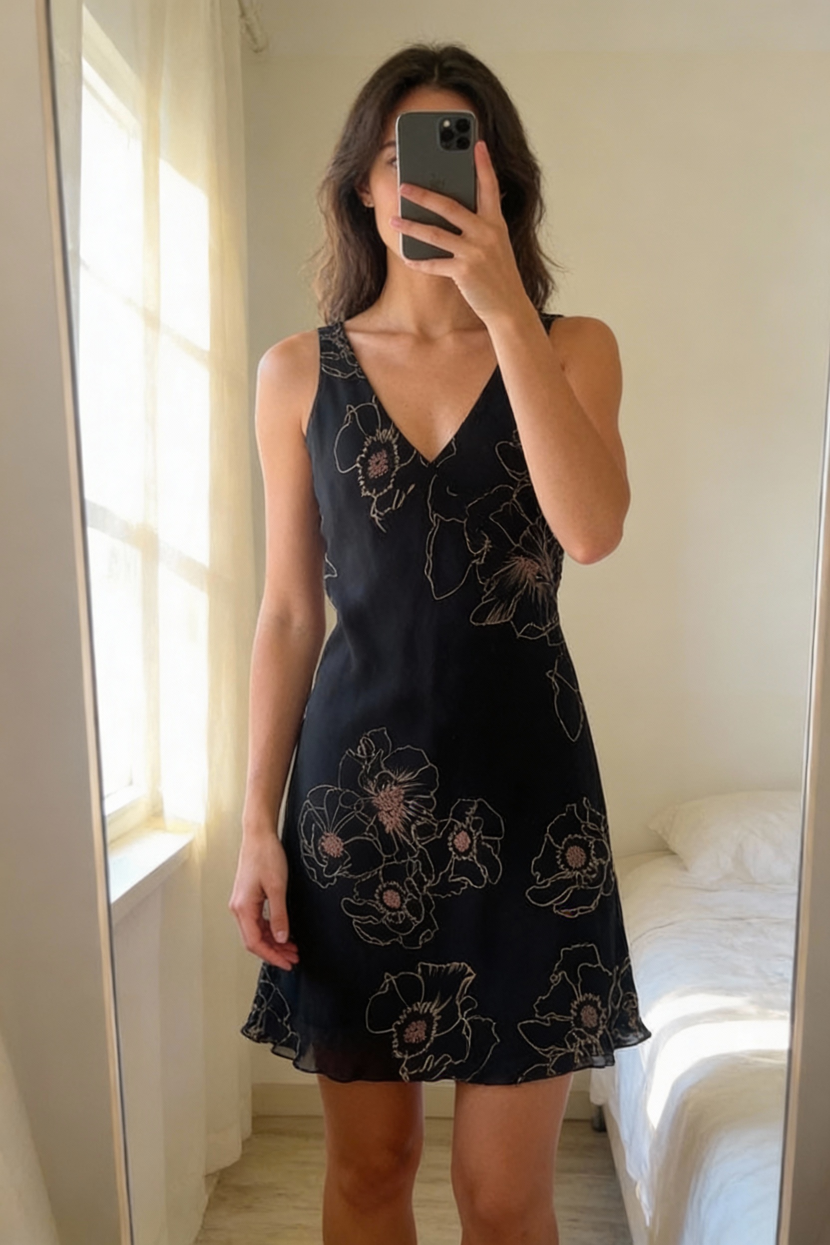A person in Vintage Y2K Jasper conran black floaty midi dress standing straight facing the camera, in a softly lit bedroom setting, with gentle natural light filtering through a window.