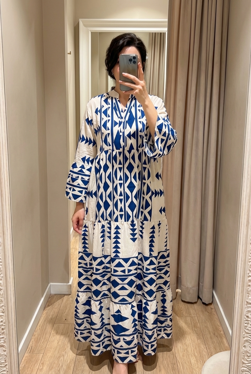 Une personne en Robe longue pour femme debout, face à la caméra, dans une cabine d’essayage de style boutique avec un miroir et une décoration neutre.