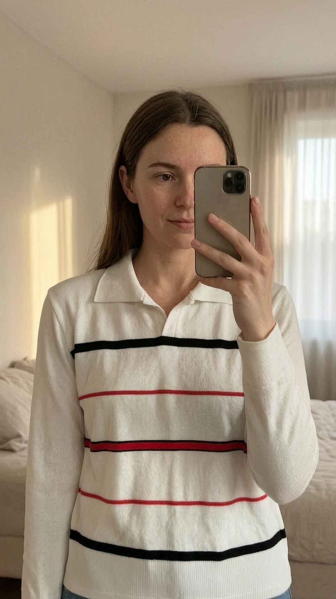 Vintage Y2K Striped Knit Polo Long Sleeve White Red Black - Size S in piedi, rivolto verso la fotocamera, in una camera da letto con luce soffusa e luce naturale che filtra dalla finestra.