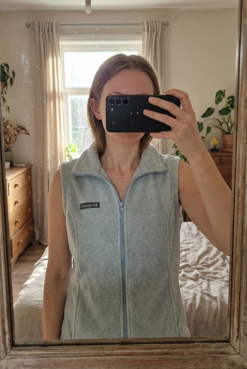 Polaire femme sans columbia debout, face à la caméra, dans une chambre à la lumière douce, avec une lumière naturelle filtrant par la fenêtre.