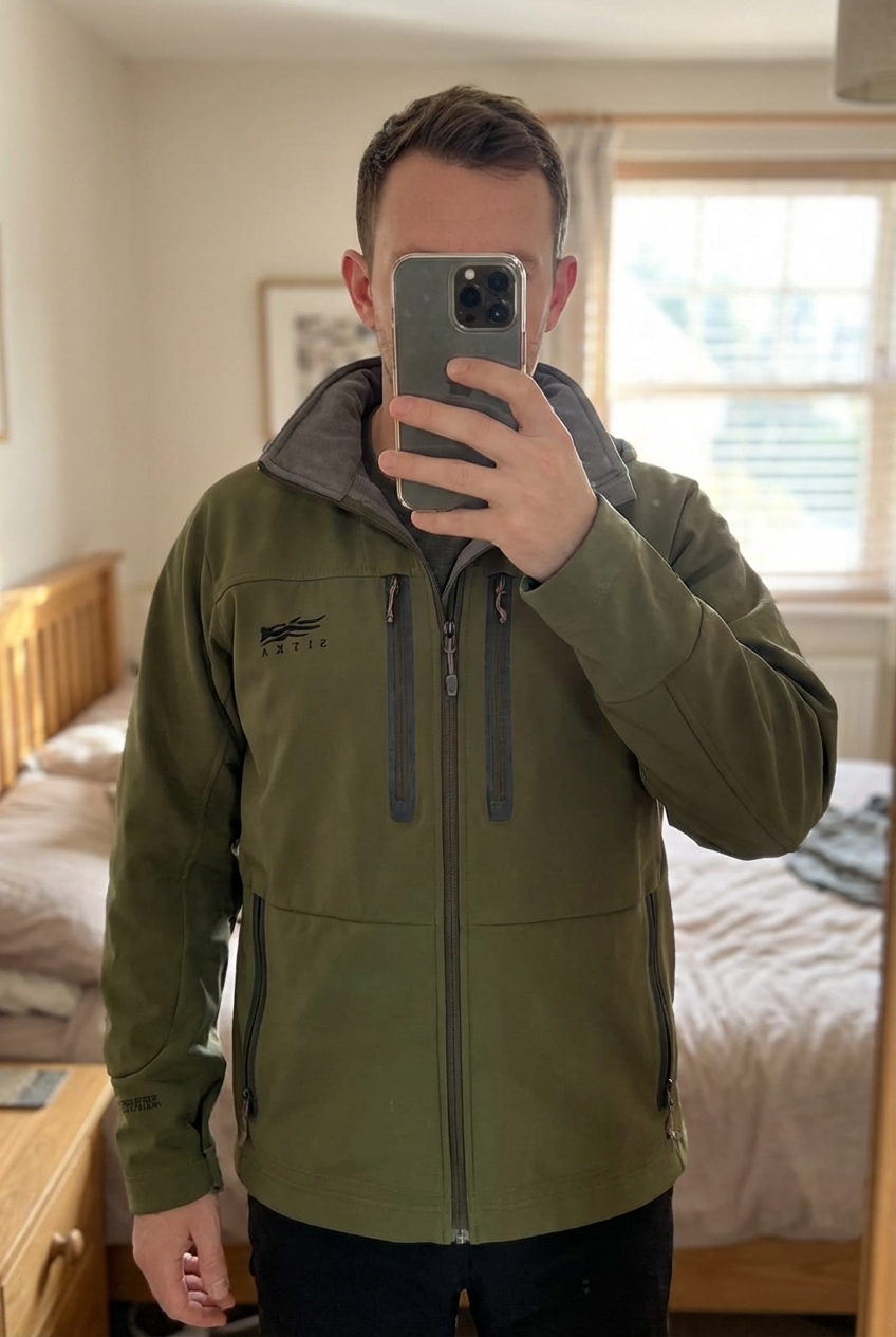 Blouson Sitka Jet Stream Gore-Tex Infinium Outdoor XL de pie, mirando a la cámara, en un dormitorio con luz suave y natural filtrándose por la ventana.