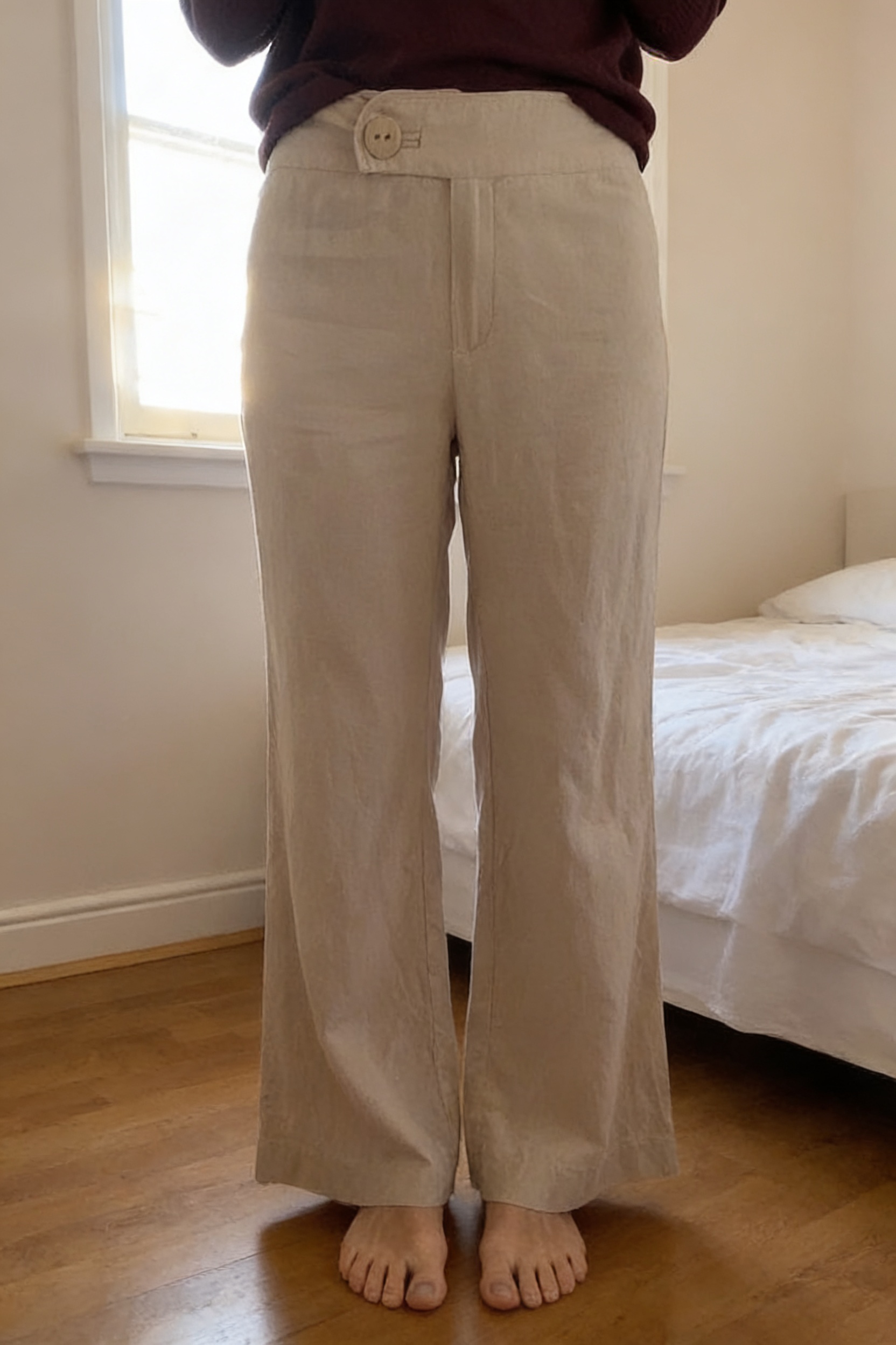 Linen and Viscose Sand Wide Leg Trousers standing straight facing the camera, in a softly lit bedroom setting, with gentle natural light filtering through a window.