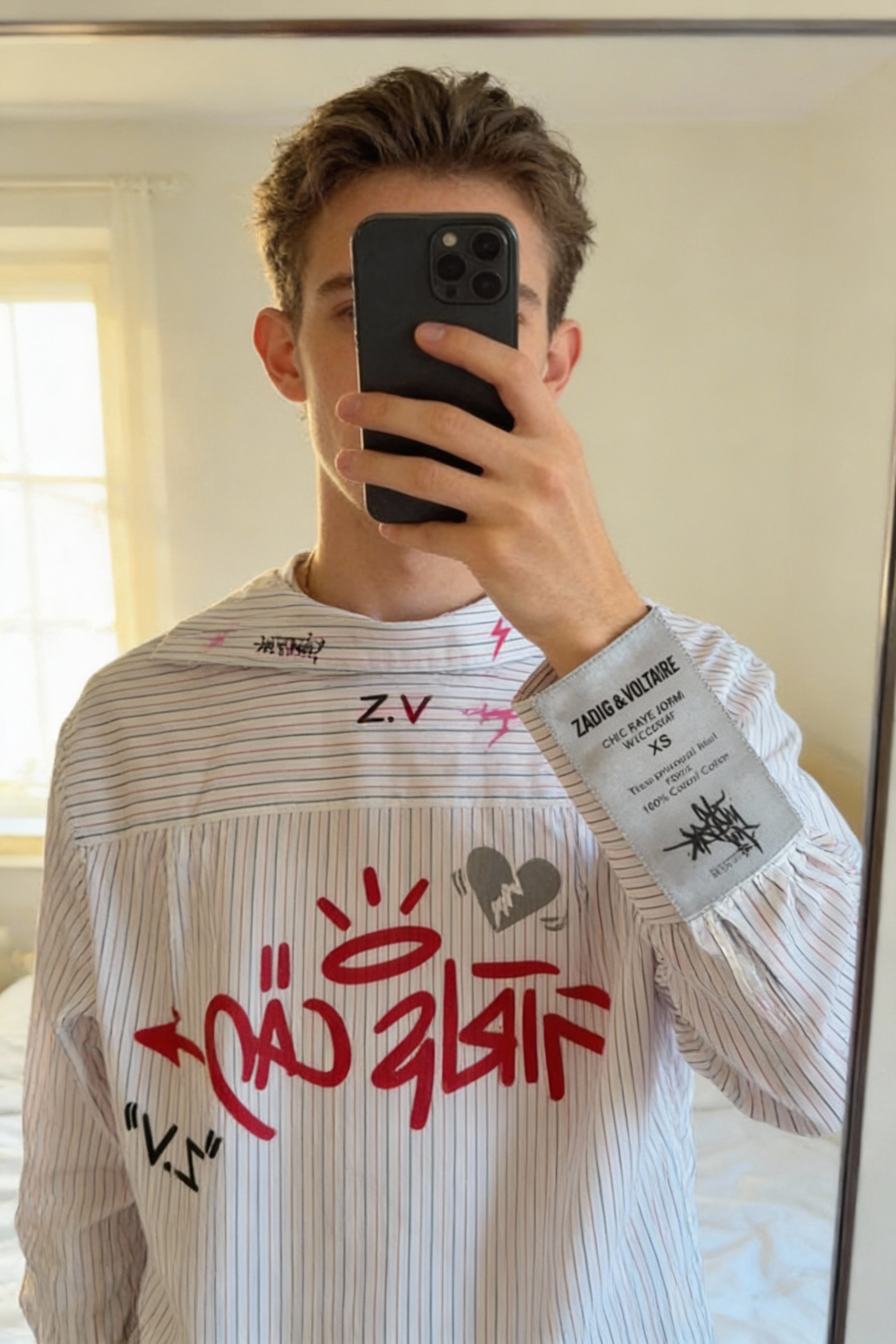 Chemise Zadig & Voltaire debout, face à la caméra, dans une chambre à la lumière douce, avec une lumière naturelle filtrant par la fenêtre.