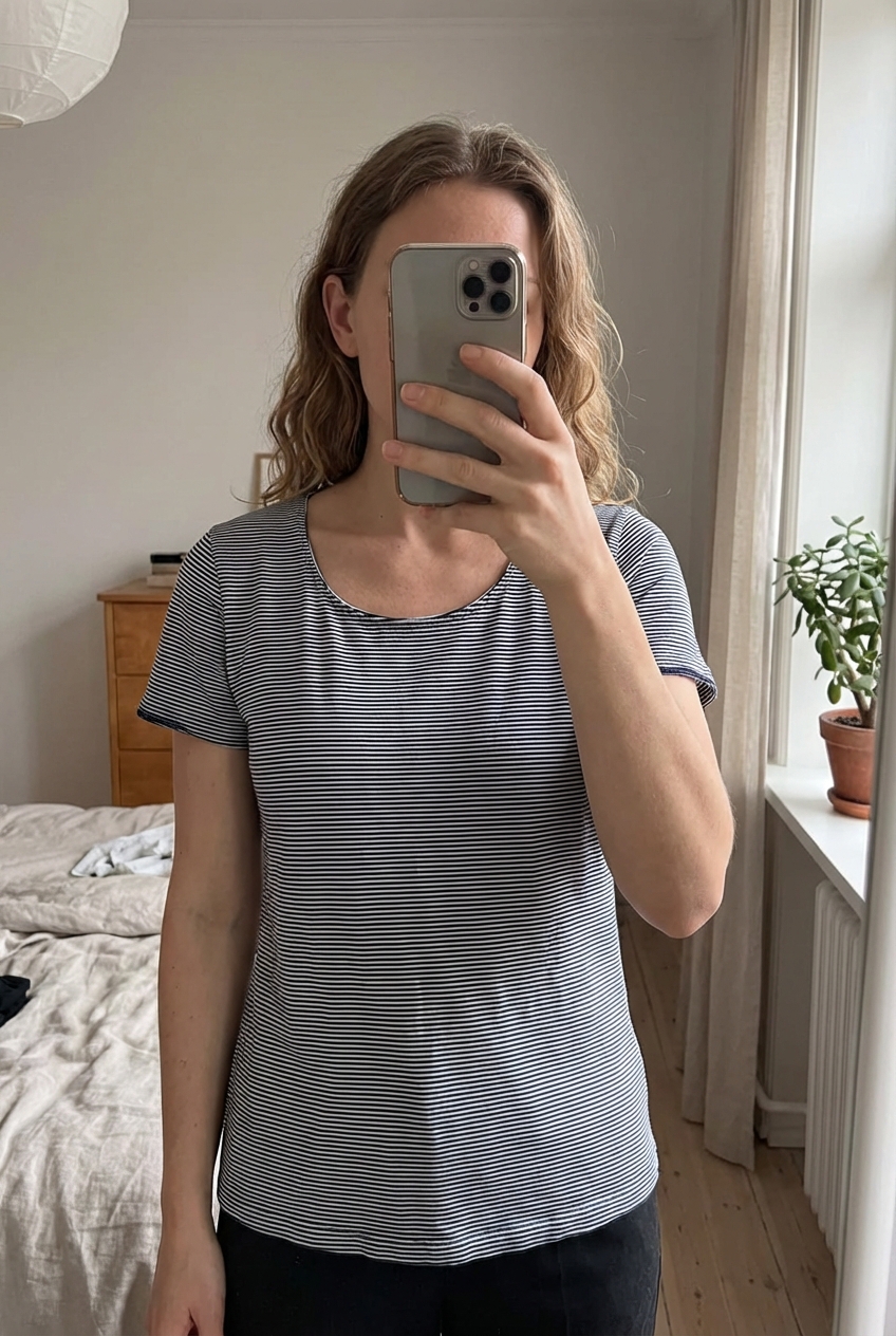 Tee shirt femme guitare taille m debout, face à la caméra, dans une chambre à la lumière douce, avec une lumière naturelle filtrant par la fenêtre.