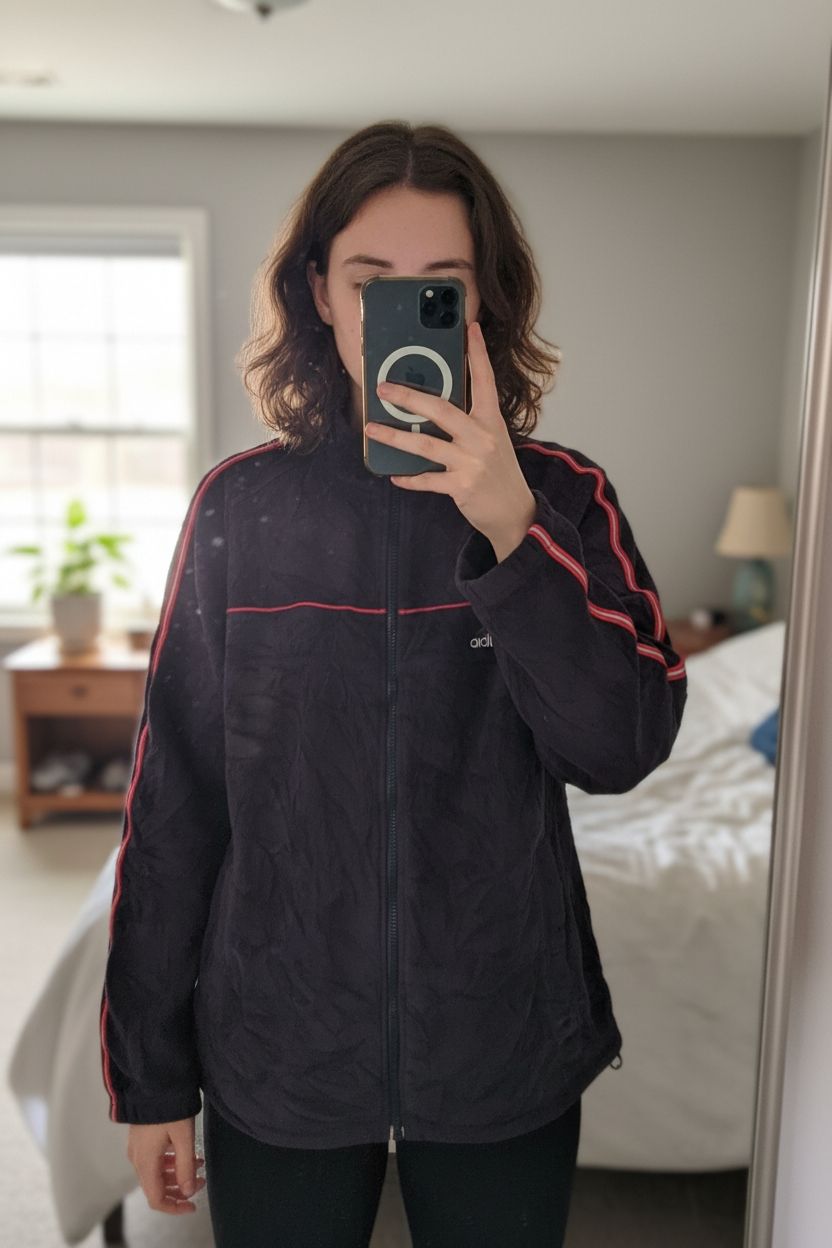 Polaire Adidas debout, face à la caméra, dans une chambre à la lumière douce, avec une lumière naturelle filtrant par la fenêtre.