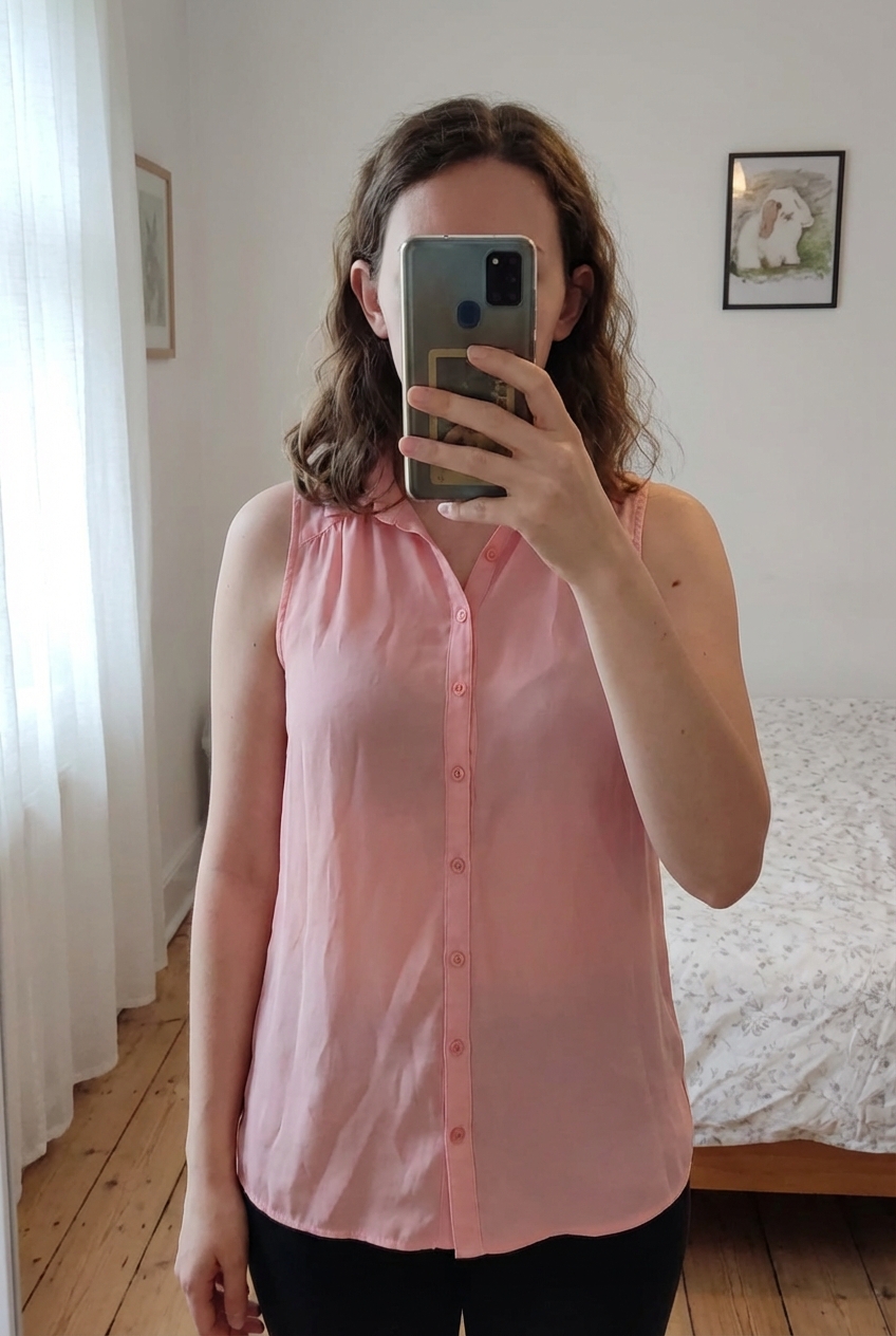 Blusa o camisa salmón de pie, mirando a la cámara, en un dormitorio con luz suave y natural filtrándose por la ventana.