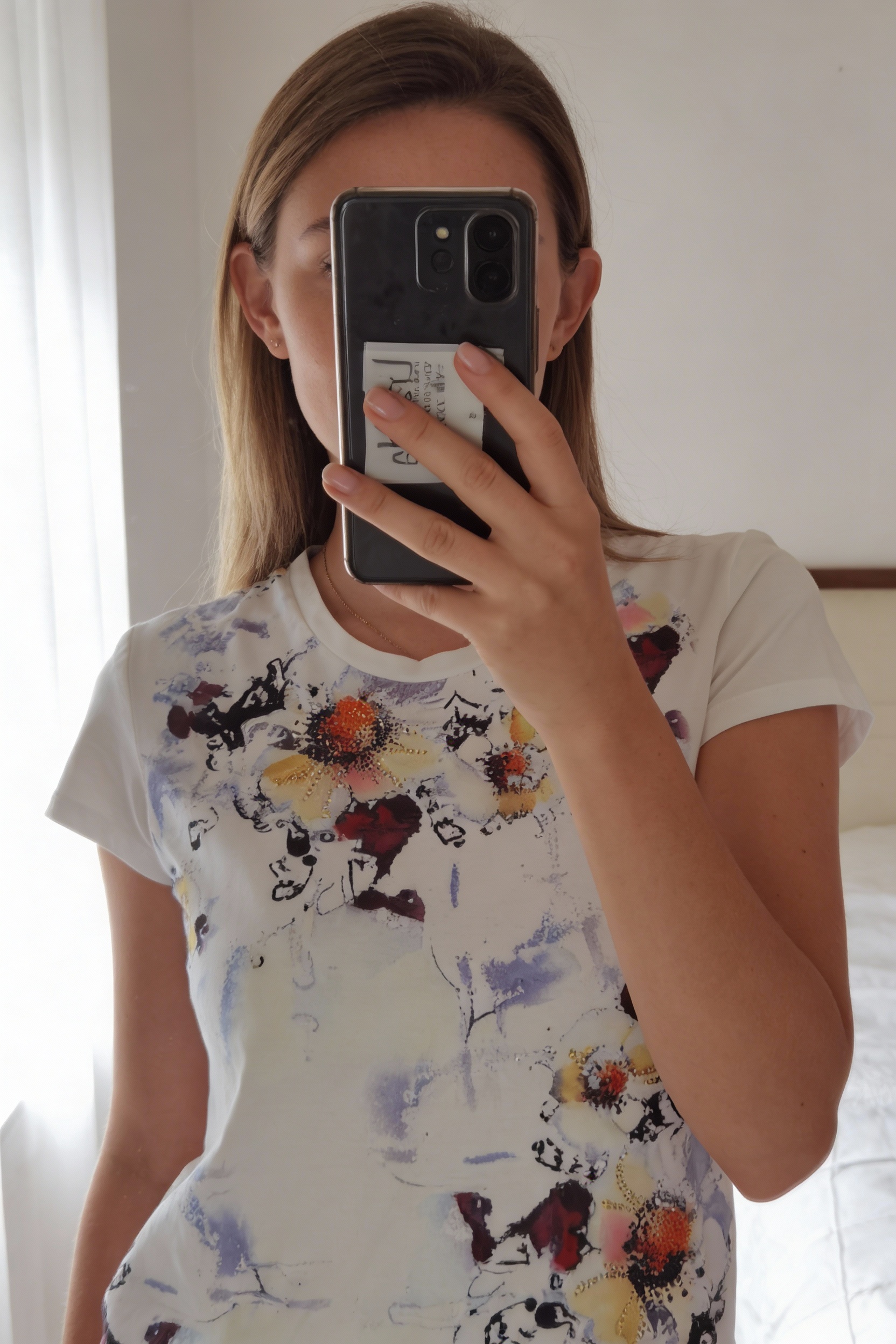 T Shirt Tattoo S debout, face à la caméra, dans une chambre à la lumière douce, avec une lumière naturelle filtrant par la fenêtre.