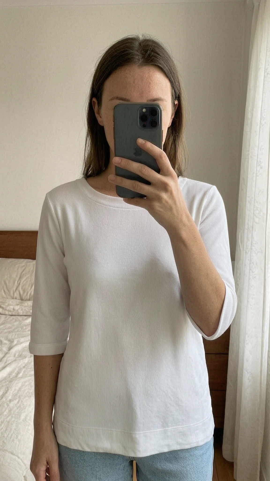 Marinière blanche petites cotes 100% coton T 42 debout, face à la caméra, dans une chambre à la lumière douce, avec une lumière naturelle filtrant par la fenêtre.