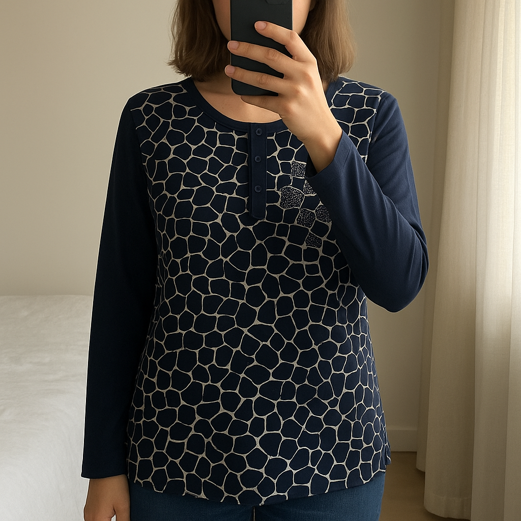 Haut imprimé noir et beige taille M debout, face à la caméra, dans une chambre à la lumière douce, avec une lumière naturelle filtrant par la fenêtre.