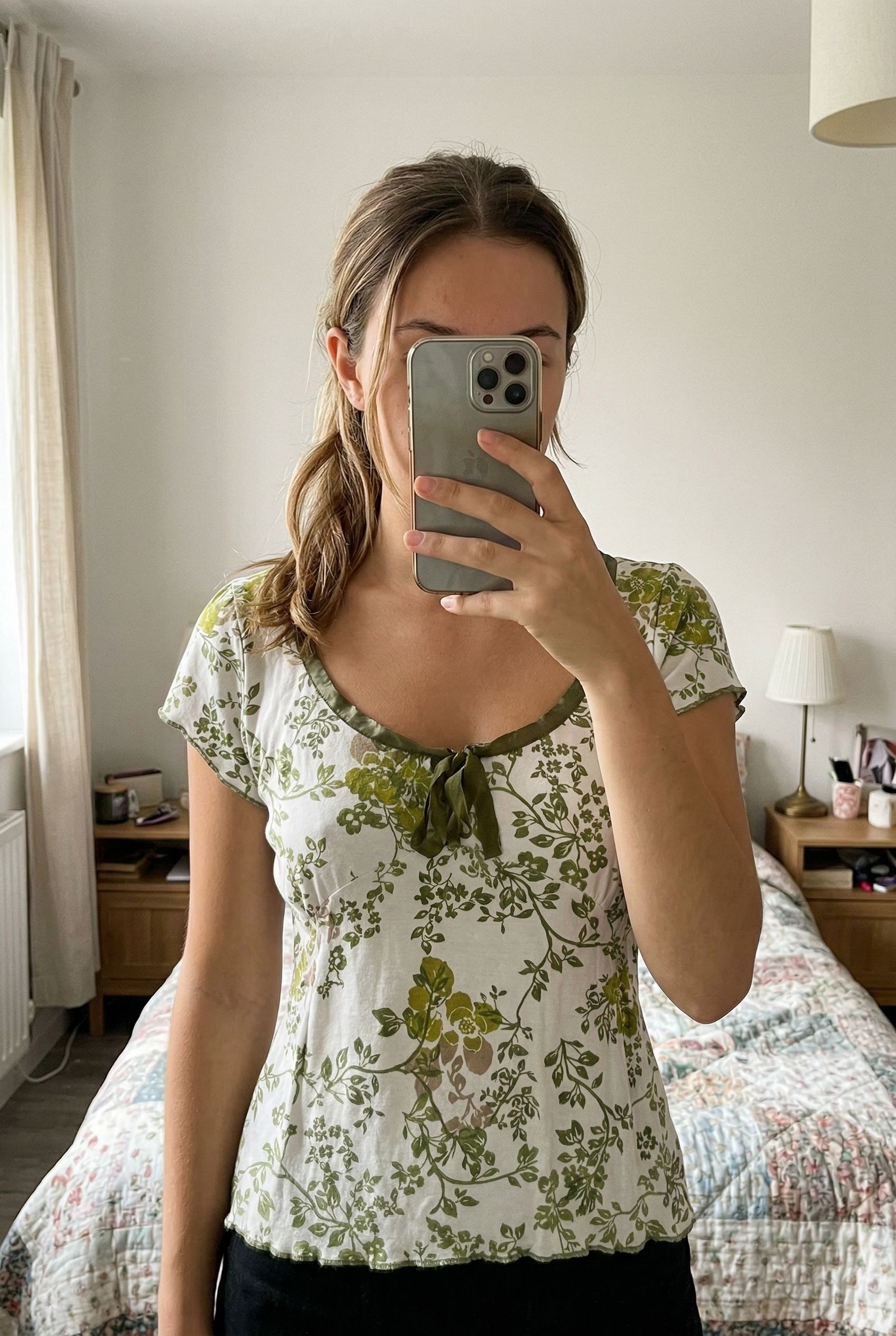 A person in Vintage Y2K per Una white & Green Tshirt standing straight facing the camera, in a softly lit bedroom setting, with gentle natural light filtering through a window.