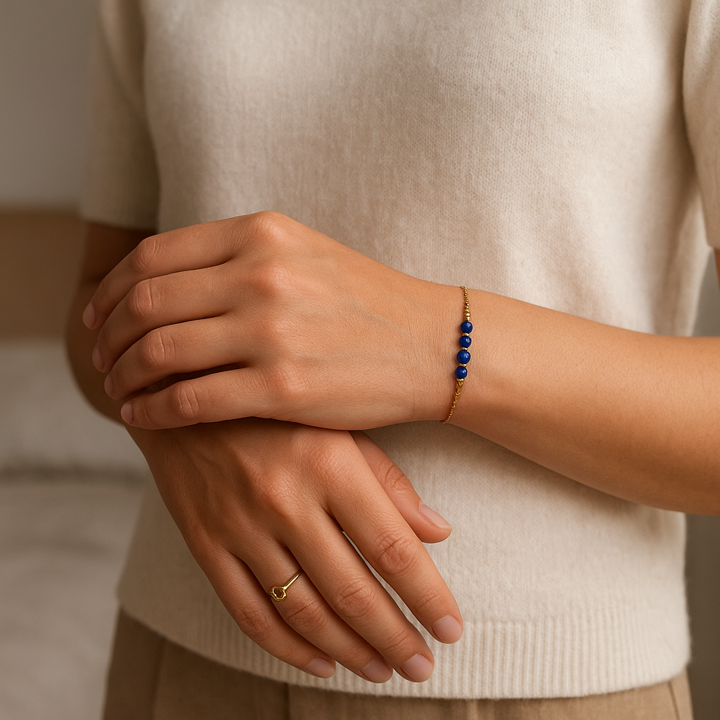 Bracelet chaine délicate dorée avec des lapis-lazulis debout, face à la caméra, dans une chambre à la lumière douce, avec une lumière naturelle filtrant par la fenêtre.