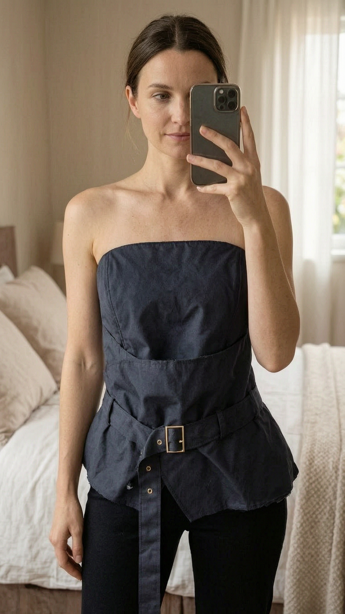 Top peplum y sin tirantes de pie, mirando a la cámara, en un dormitorio con luz suave y natural filtrándose por la ventana.