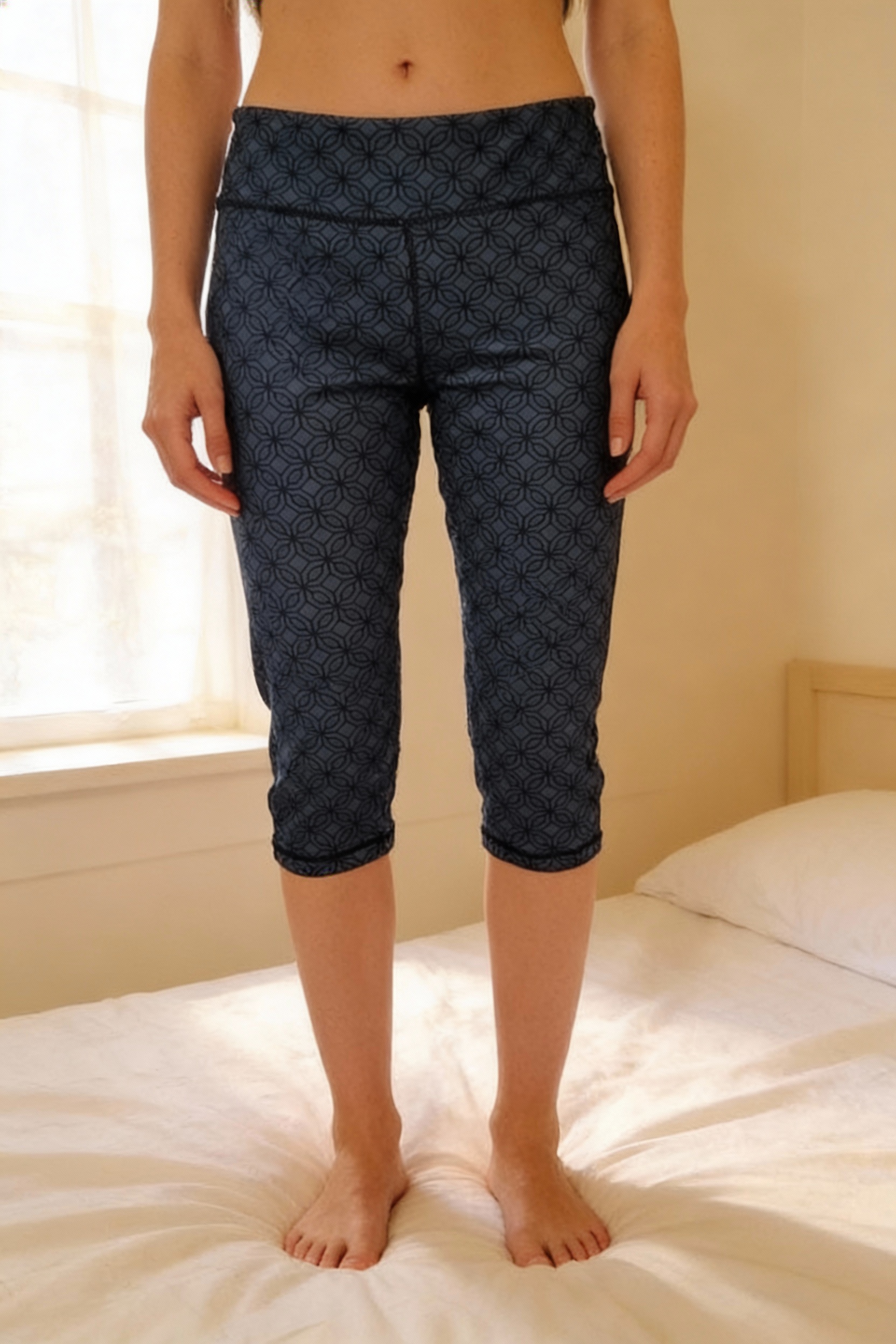 CRIVIT 3/4-length leggings standing straight facing the camera, in a softly lit bedroom setting, with gentle natural light filtering through a window.