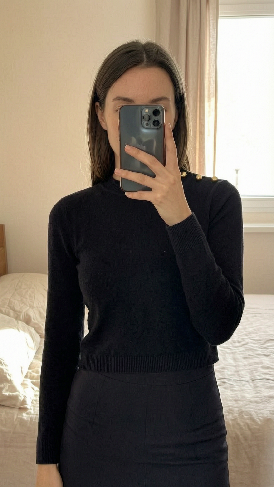 Pull Sandro taille 1 debout, face à la caméra, dans une chambre à la lumière douce, avec une lumière naturelle filtrant par la fenêtre.