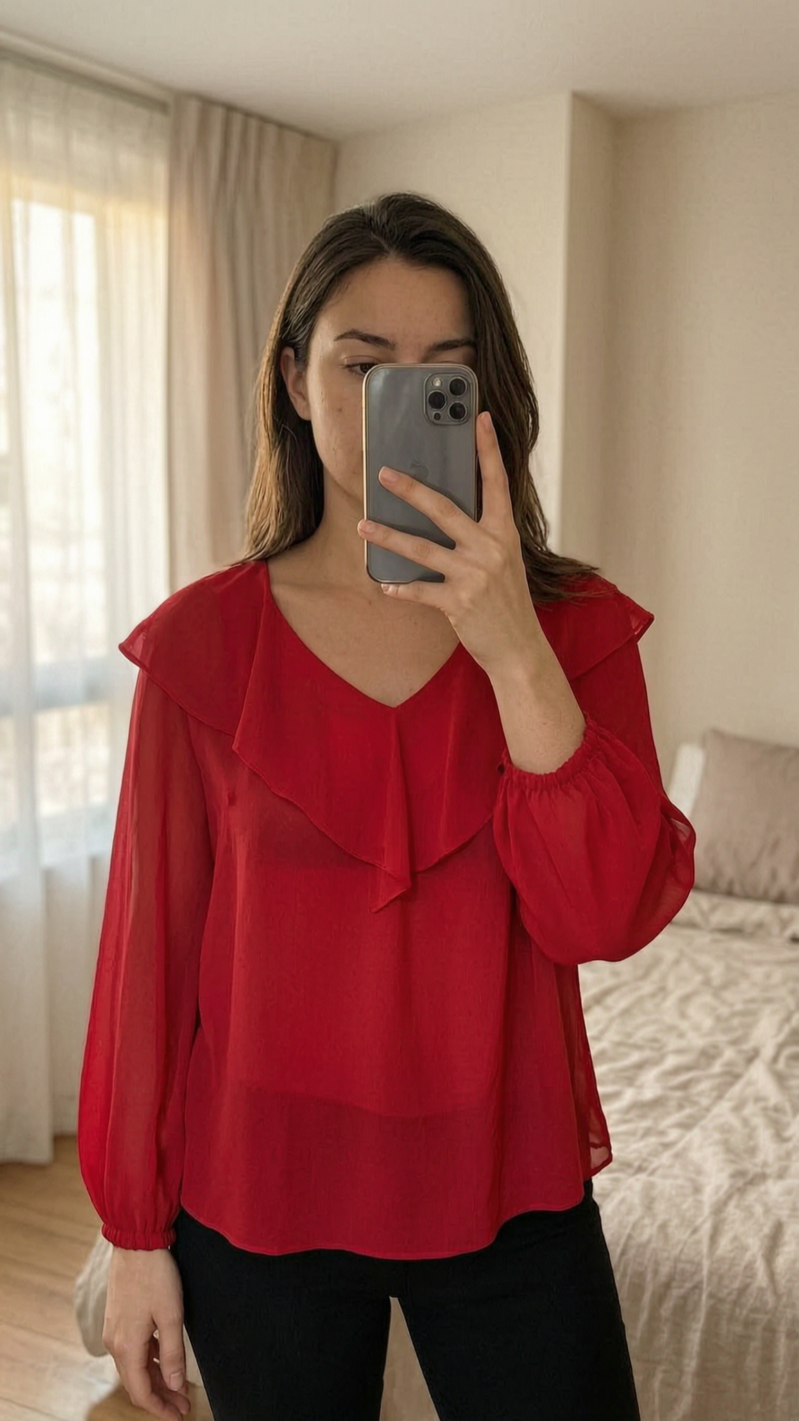 Blouse fluide rouge S debout, face à la caméra, dans une chambre à la lumière douce, avec une lumière naturelle filtrant par la fenêtre.