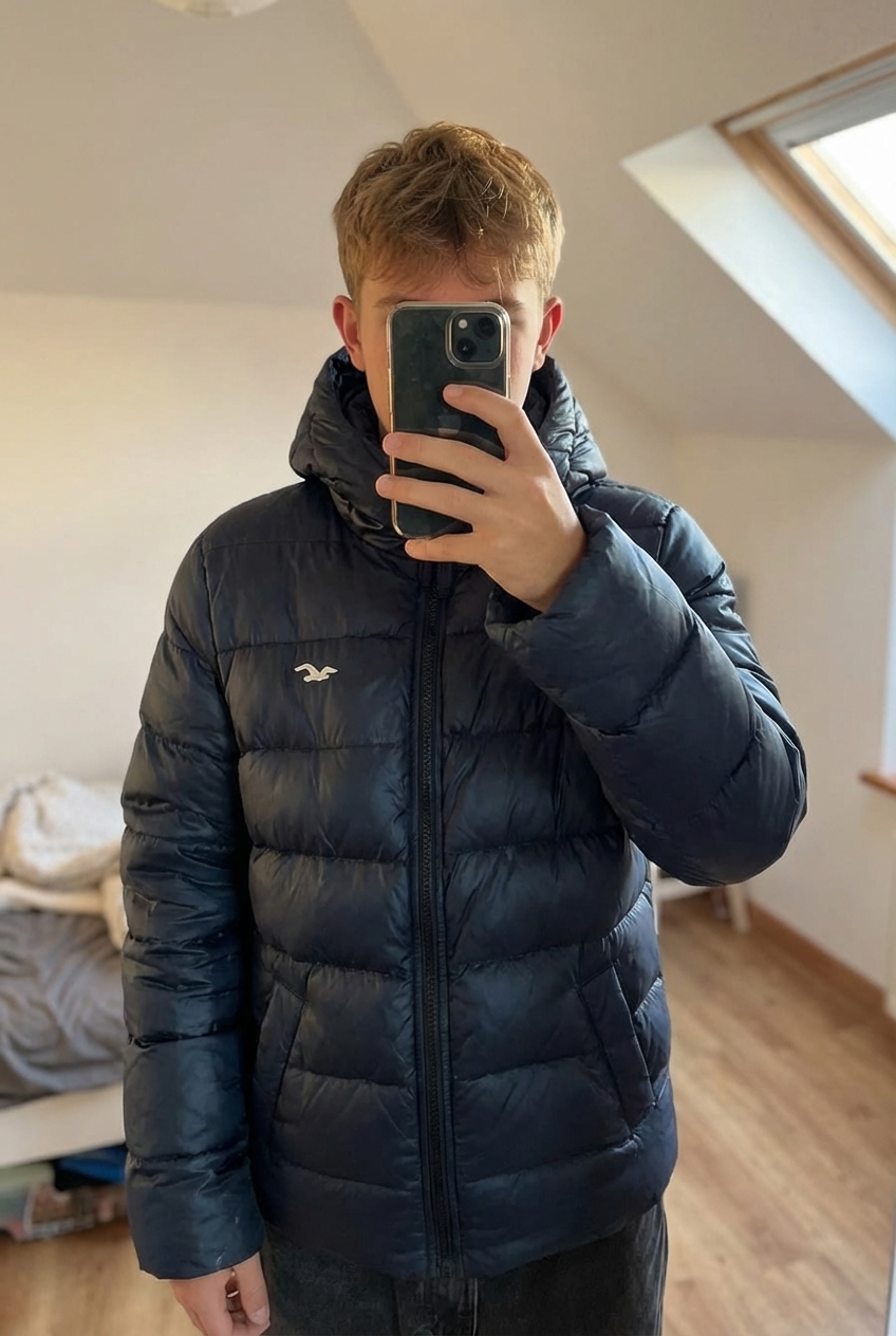 Doudoune Hollister debout, face à la caméra, dans une chambre à la lumière douce, avec une lumière naturelle filtrant par la fenêtre.